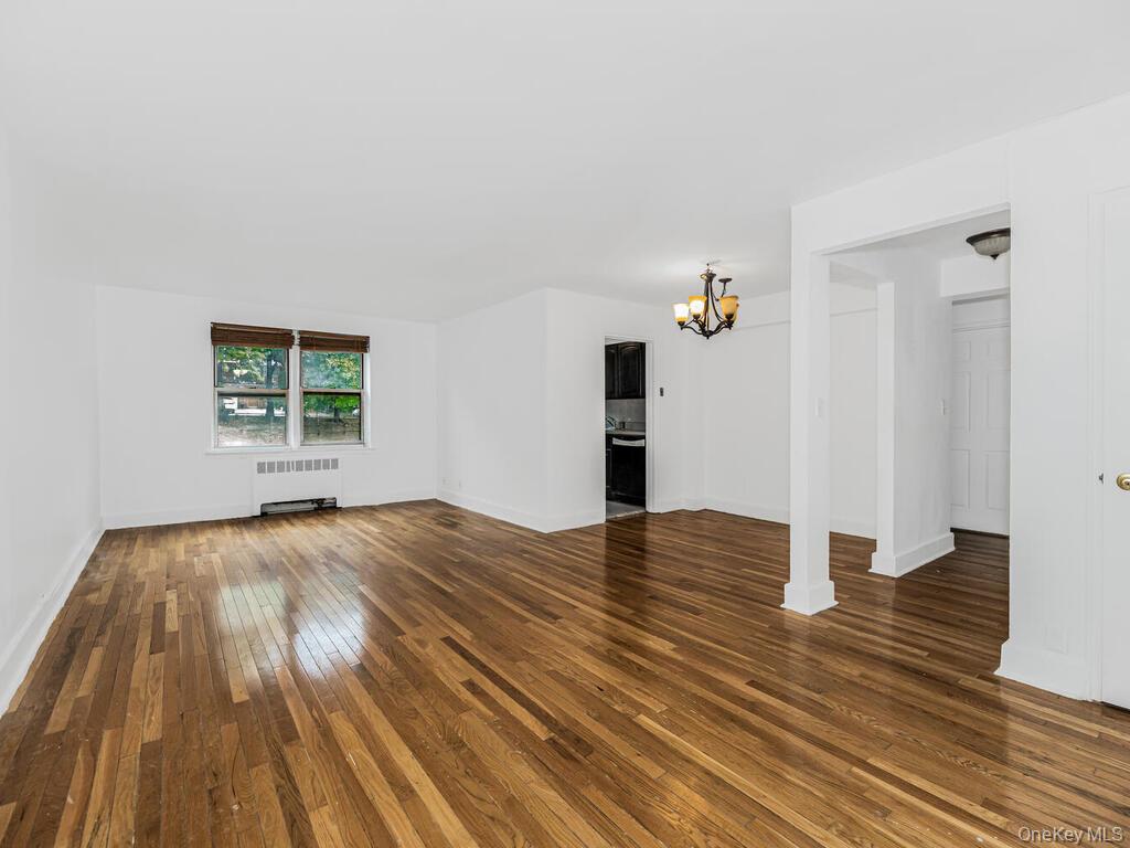Unfurnished living room featuring radiator heating unit, a chandelier, and dark hardwood / wood-style flooring