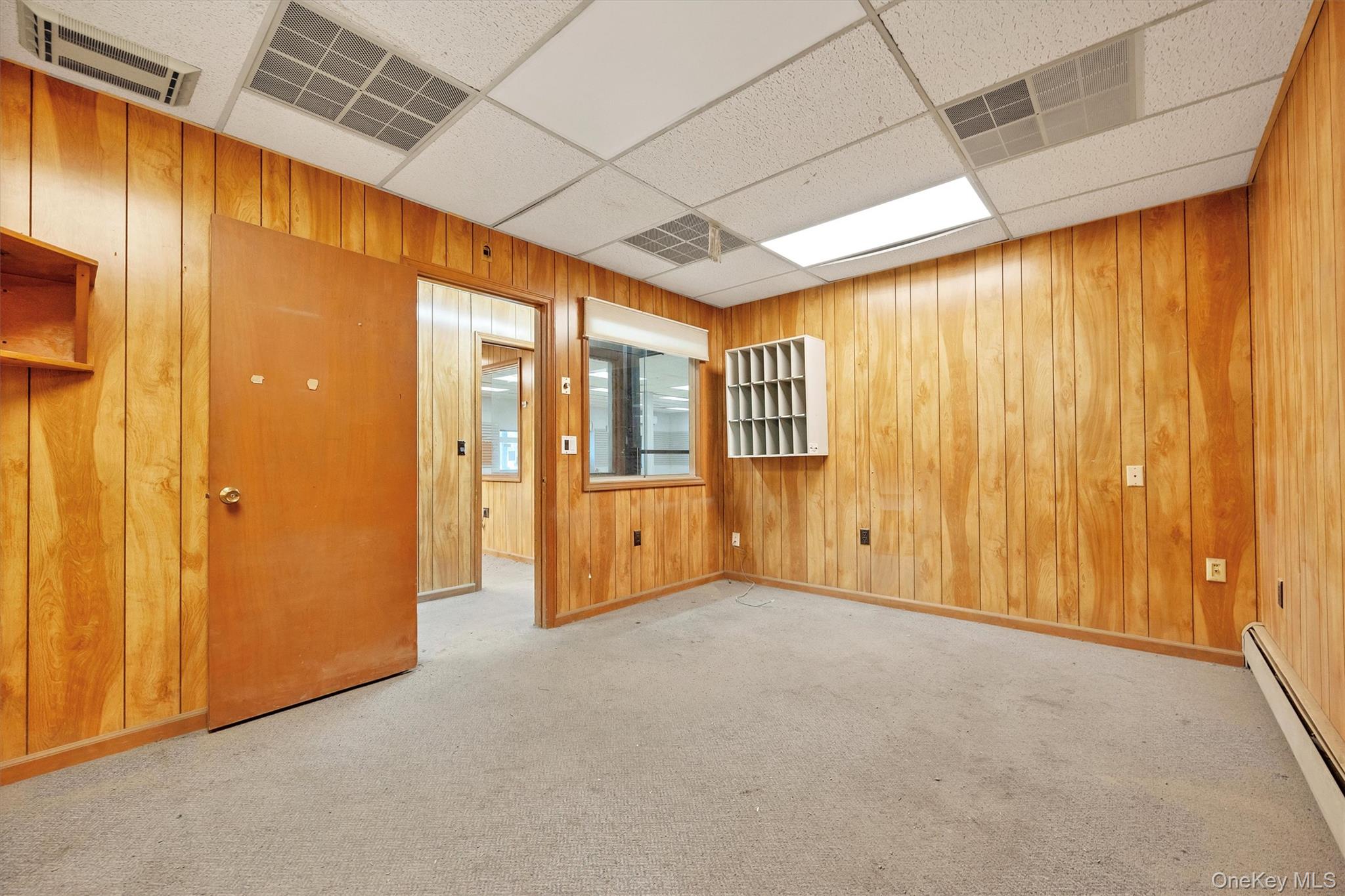 Carpeted spare room featuring a baseboard radiator, wooden walls, and a paneled ceiling