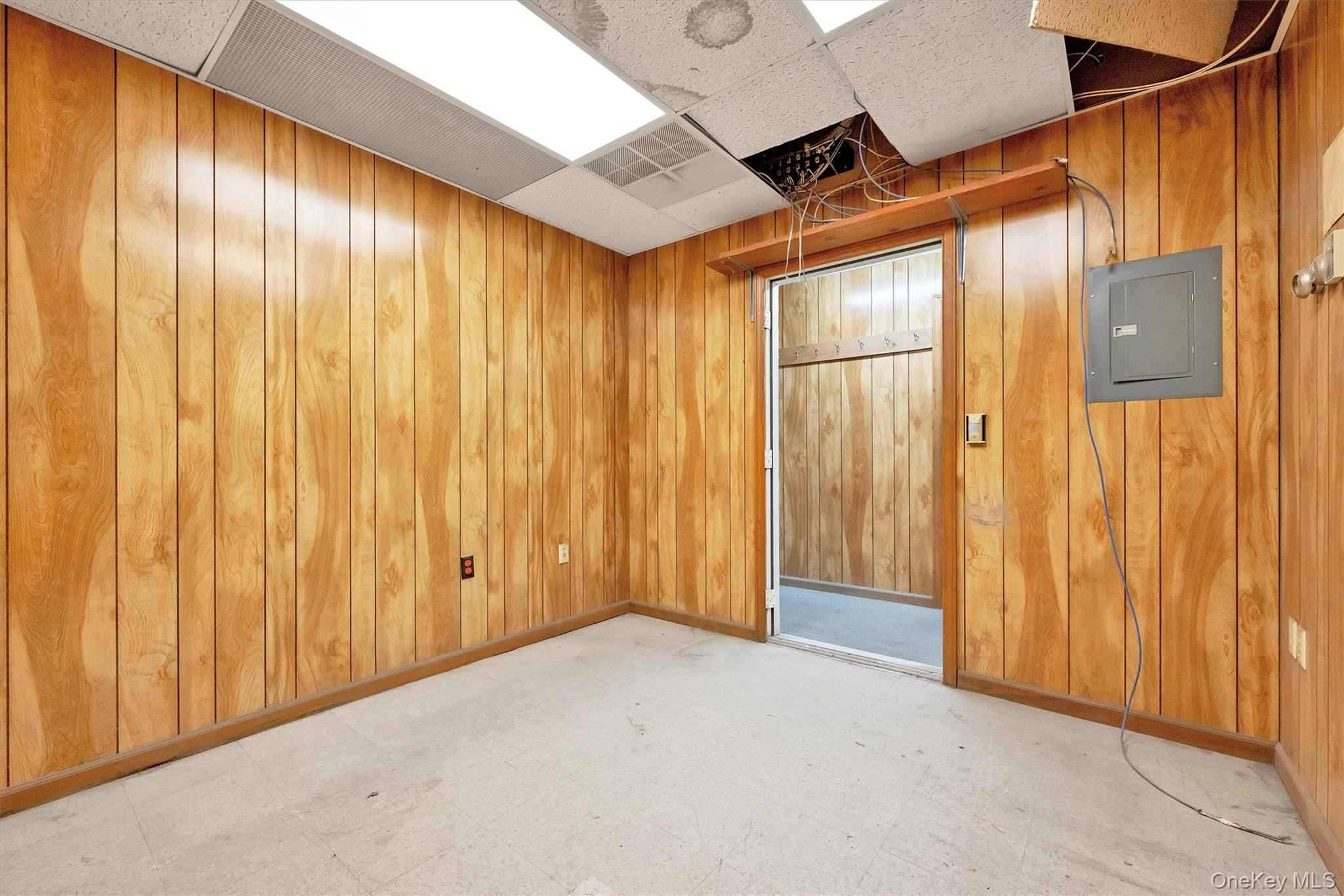 Unfurnished room with a paneled ceiling, electric panel, and wood walls