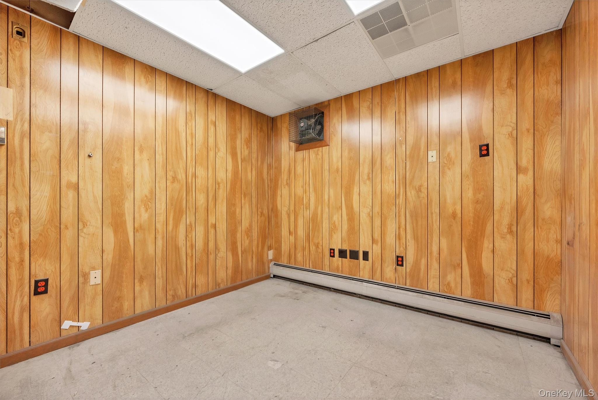 Empty room with a baseboard heating unit, a paneled ceiling, and wood walls