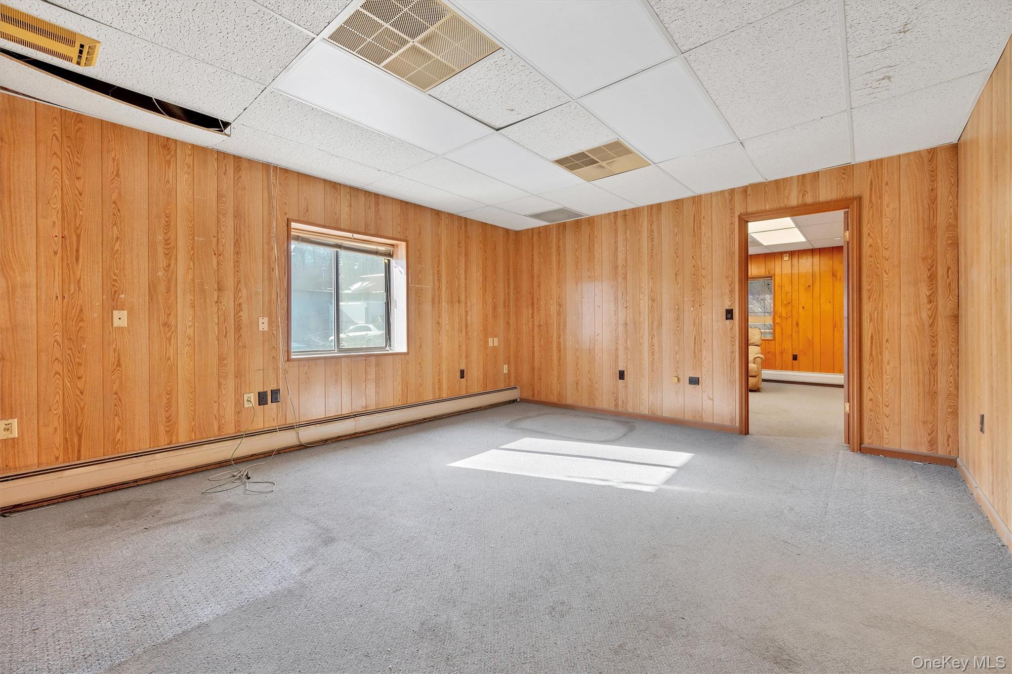 Carpeted spare room featuring a paneled ceiling, wood walls, and baseboard heating