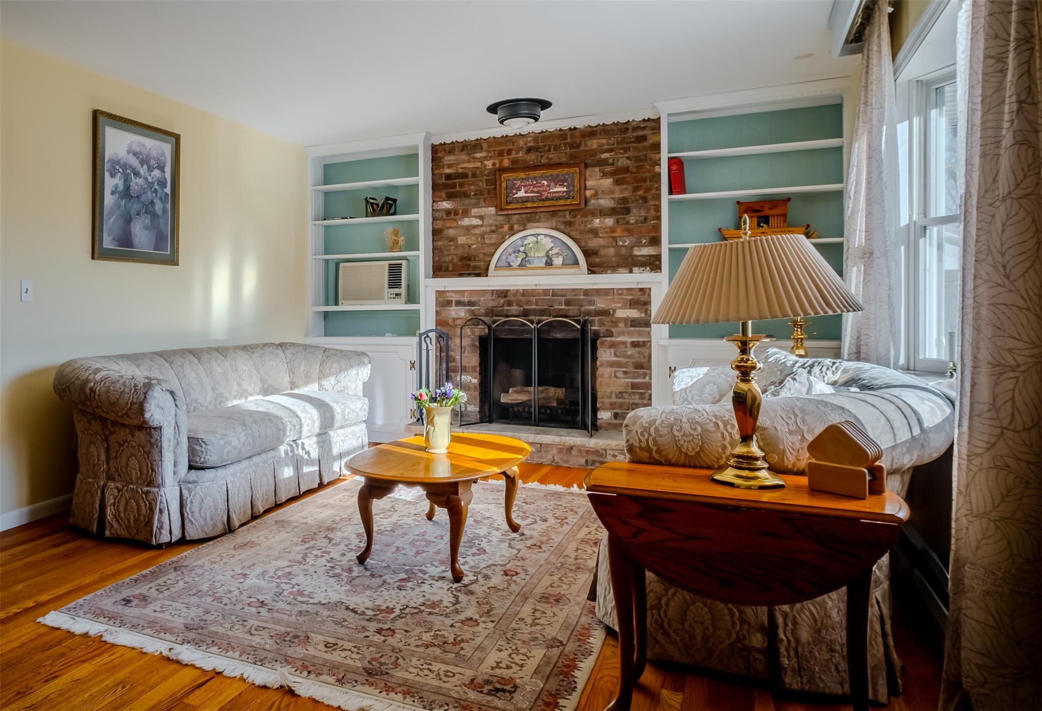 Sitting room with built in features, a brick fireplace, baseboards, and wood finished floors