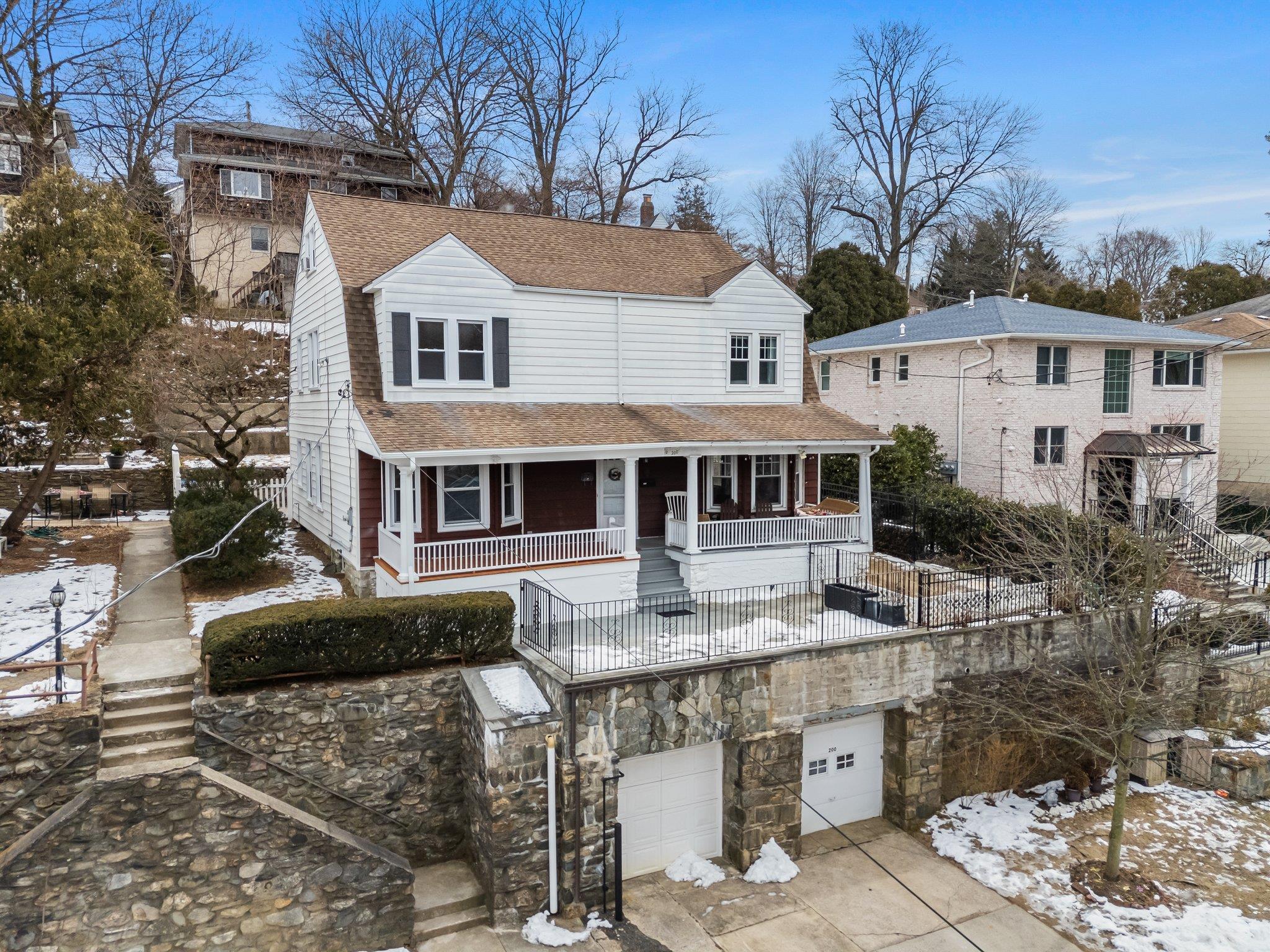Snow covered back of property featuring a shingled roof, covered porch, and an attached garage