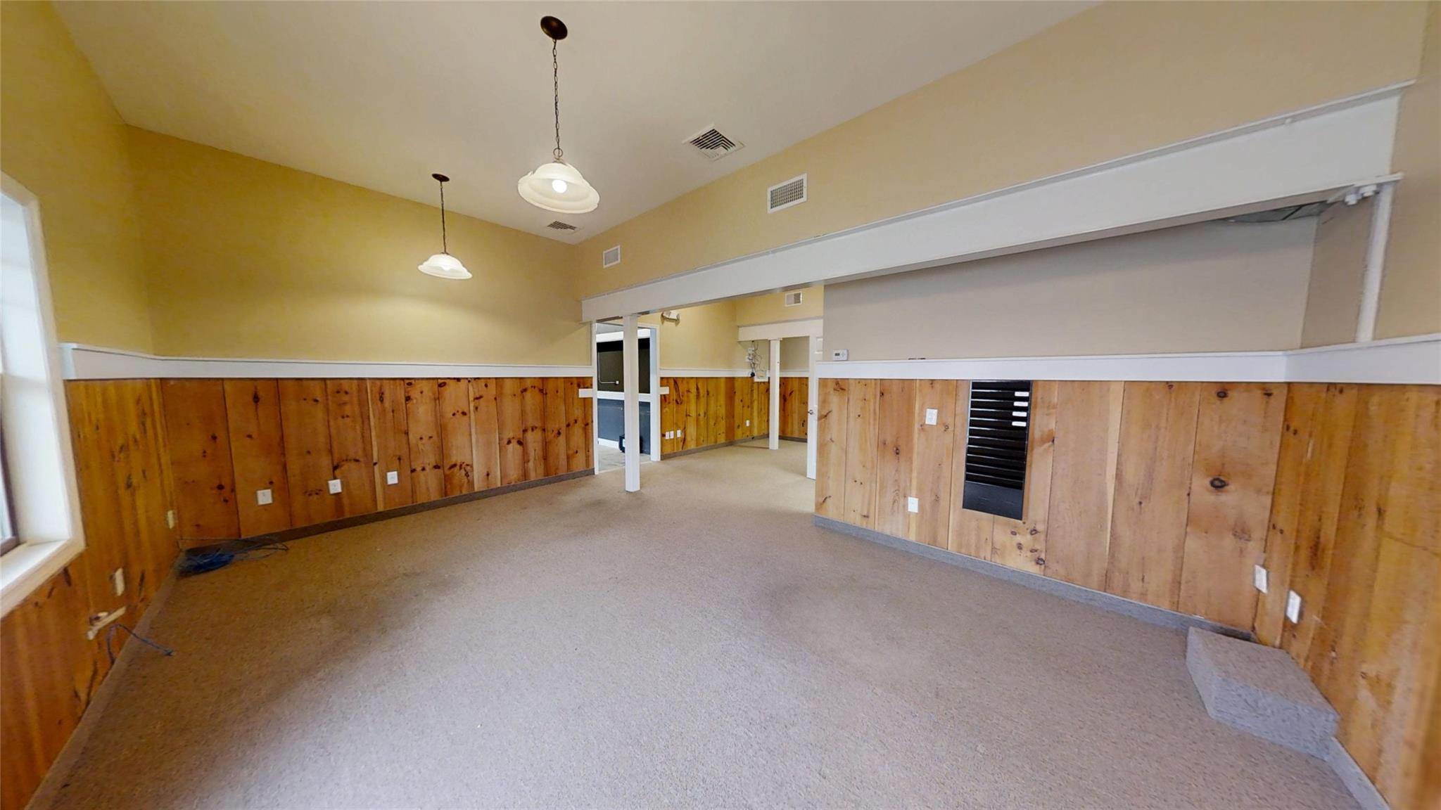 Empty room with carpet, a wainscoted wall, visible vents, and wooden walls