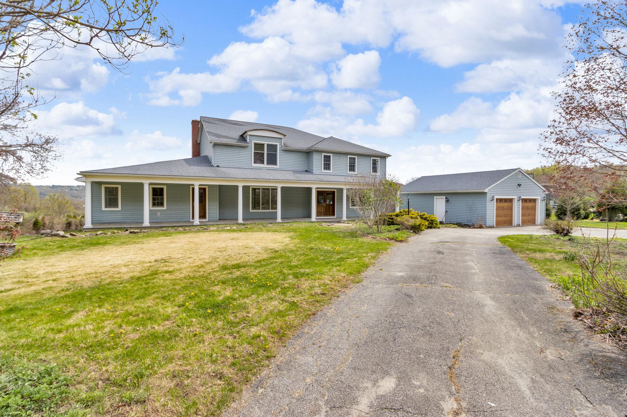 Farmhouse-style home with covered porch, driveway, a garage, and a front yard