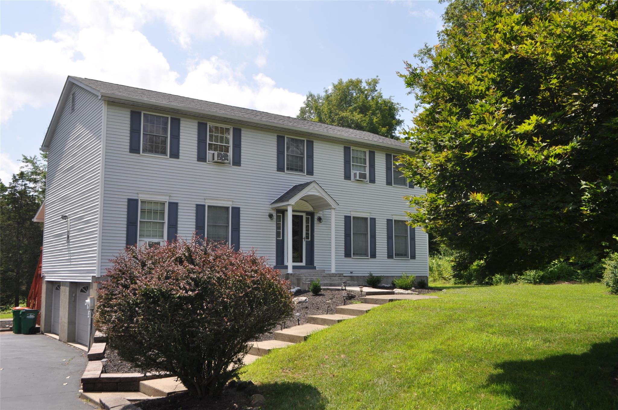 Colonial-style house featuring a garage, asphalt driveway, and a front lawn