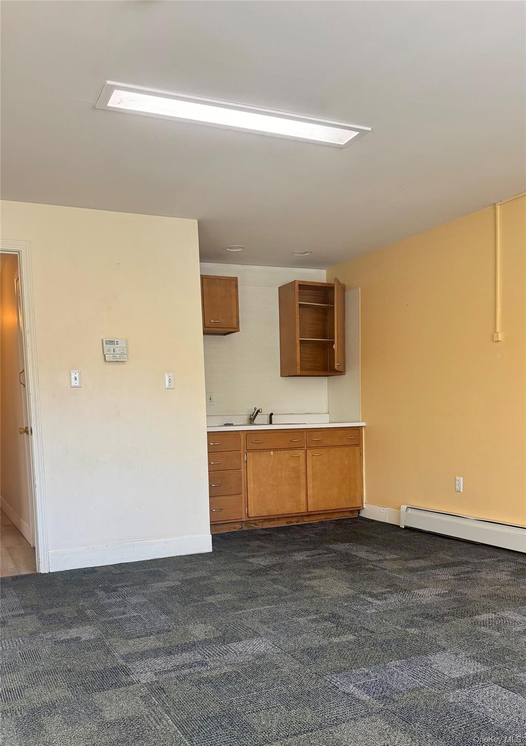 Kitchen with light countertops, brown cabinets, a baseboard radiator, dark carpet, and open shelves