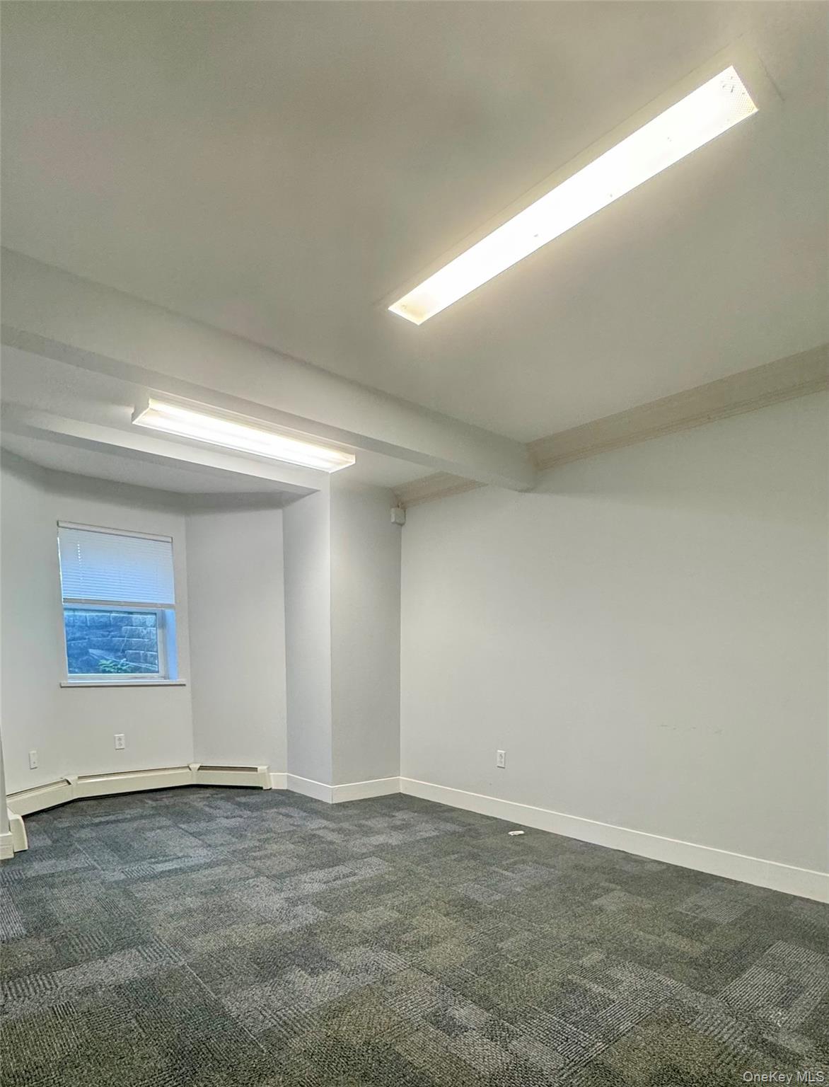 Unfurnished room with dark colored carpet, a baseboard heating unit, and beamed ceiling