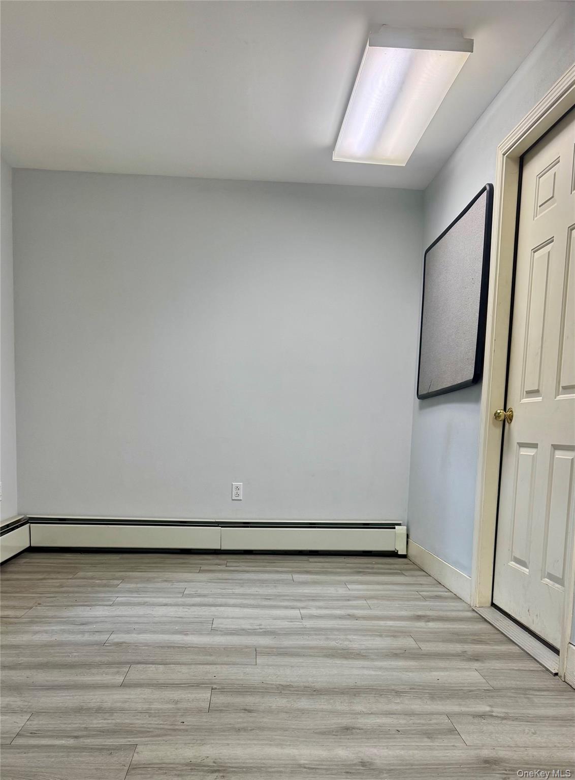 Empty room with light wood-style flooring and a baseboard heating unit