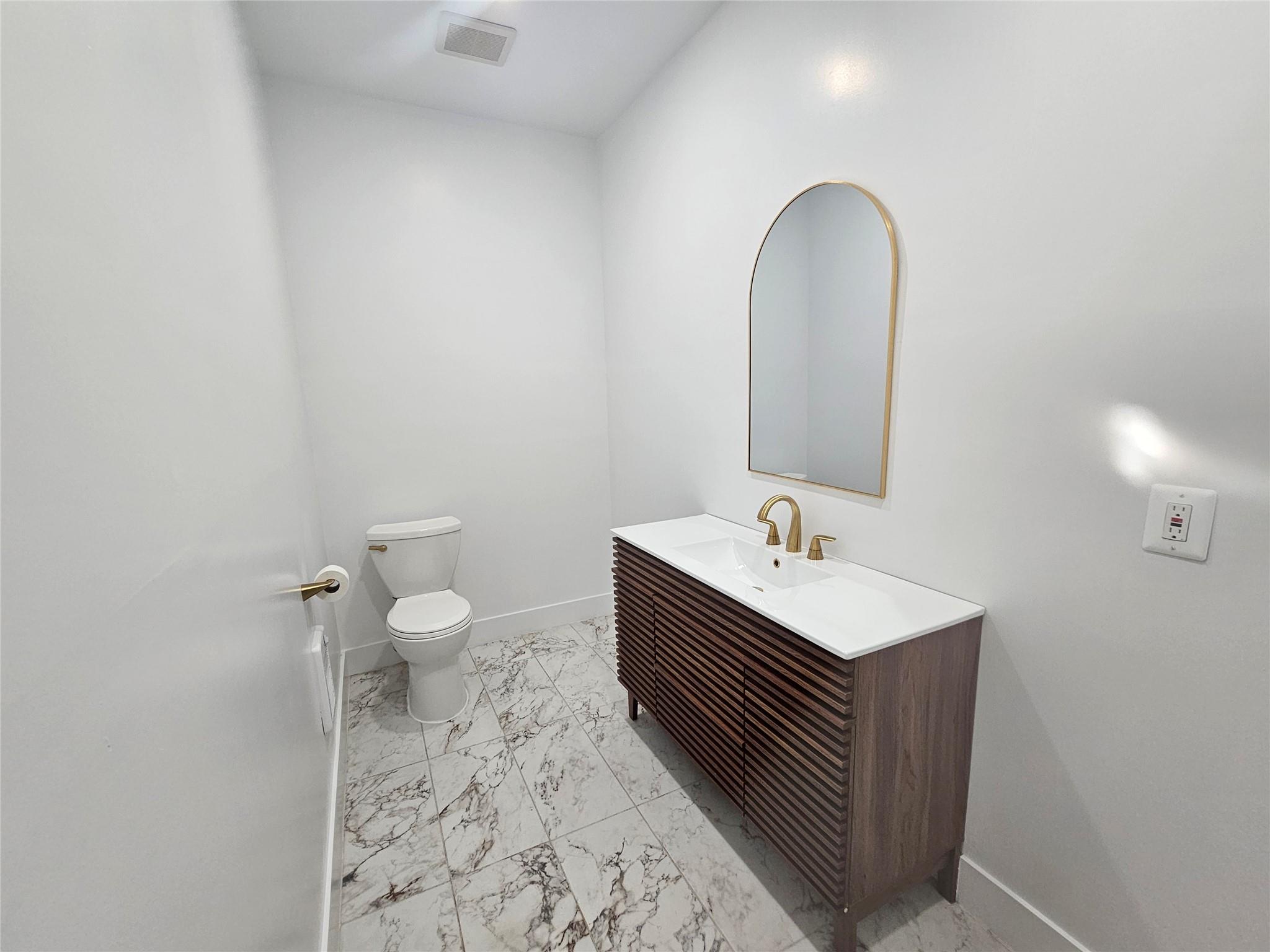 Half bathroom featuring marble finish floors, toilet, baseboards, and vanity