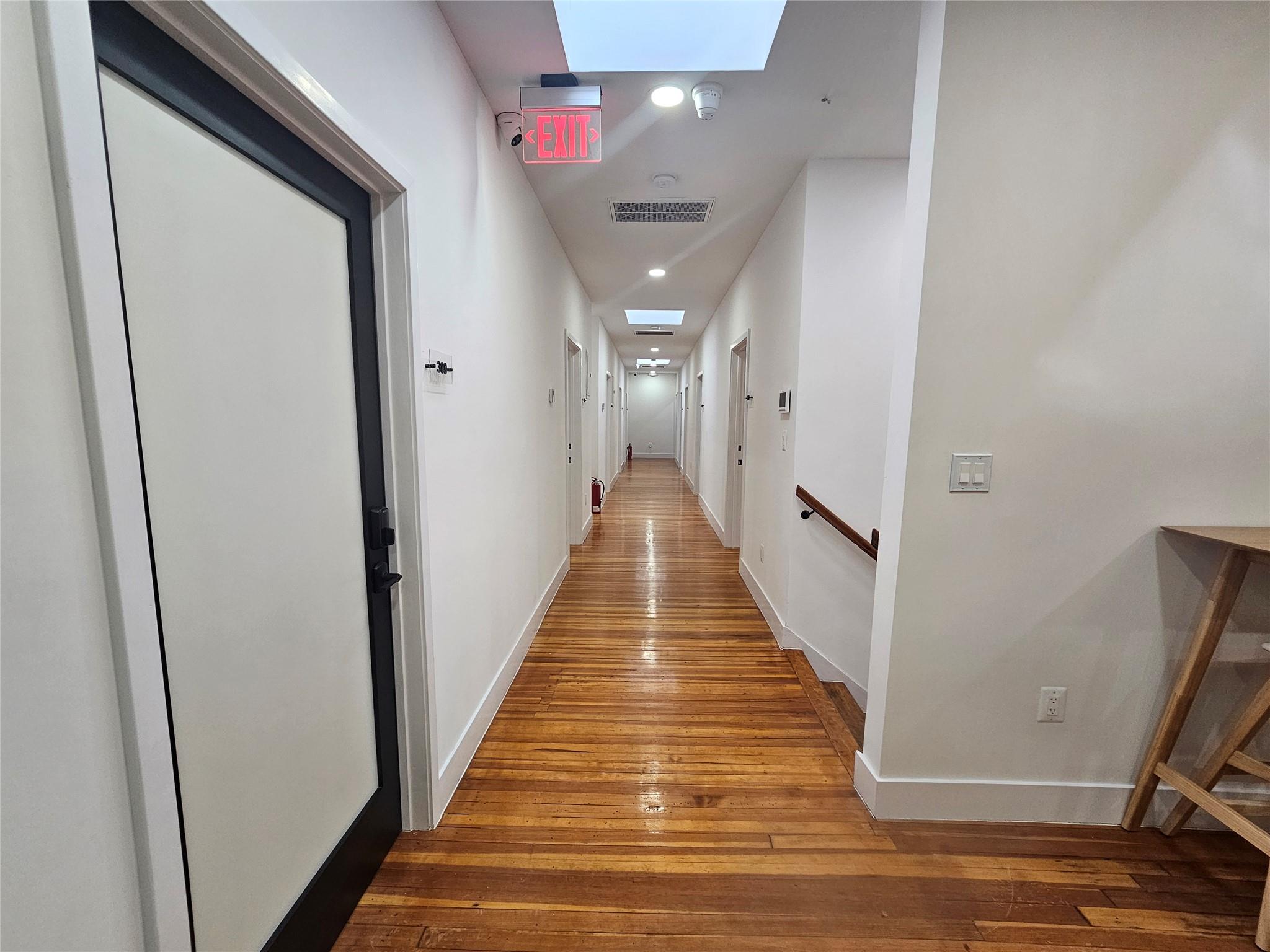 Hall with hardwood / wood-style floors, recessed lighting, baseboards, and a skylight