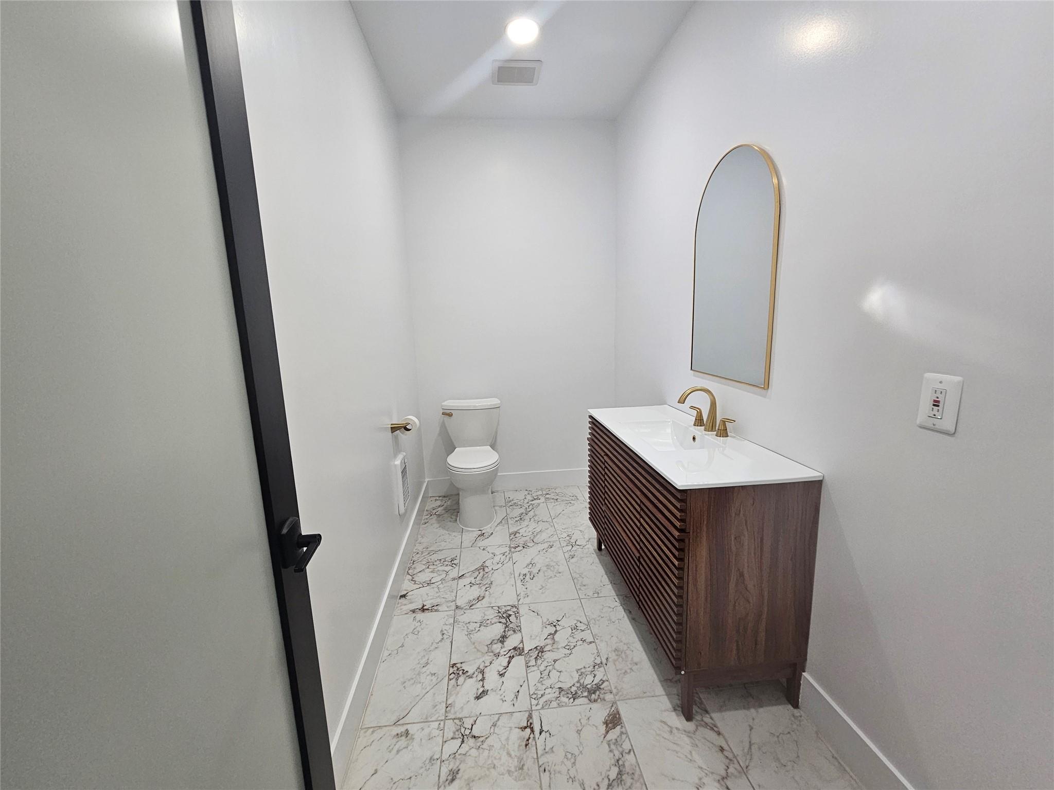 Bathroom featuring marble look tiles, baseboards, toilet, and vanity