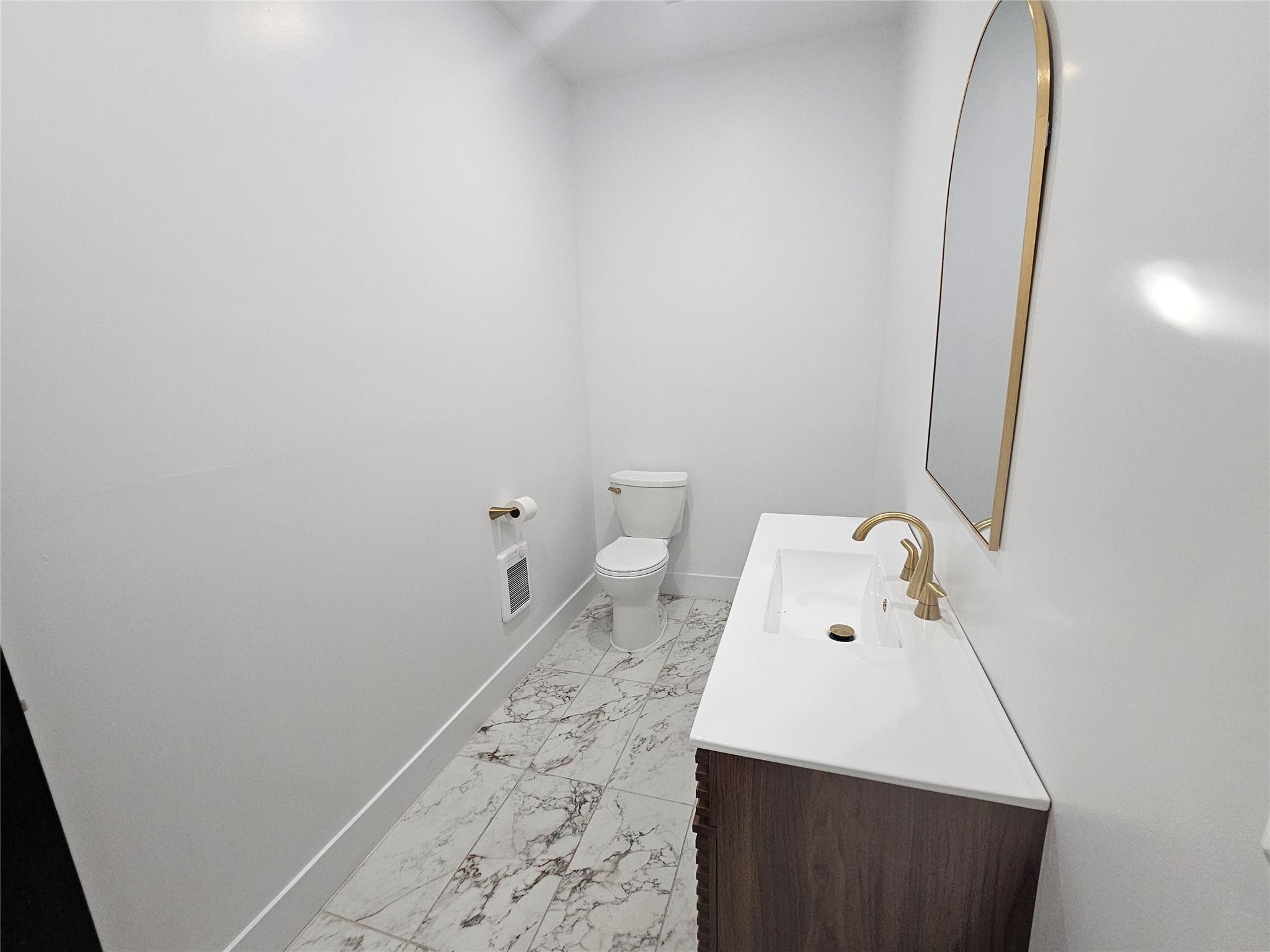 Half bath with marble look tile flooring, toilet, baseboards, and vanity