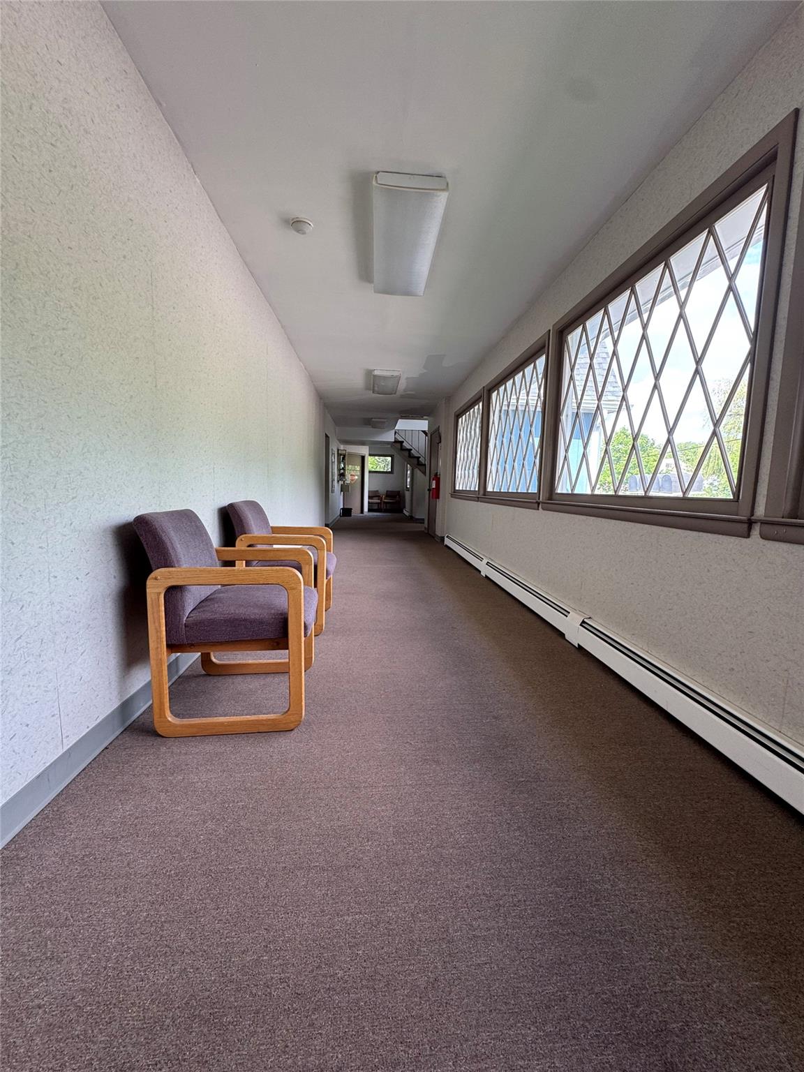 Hall with a baseboard heating unit, a textured wall, and dark carpet
