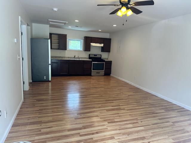 Kitchen featuring appliances with stainless steel finishes, under cabinet range hood, light wood finished floors, baseboards, and open floor plan