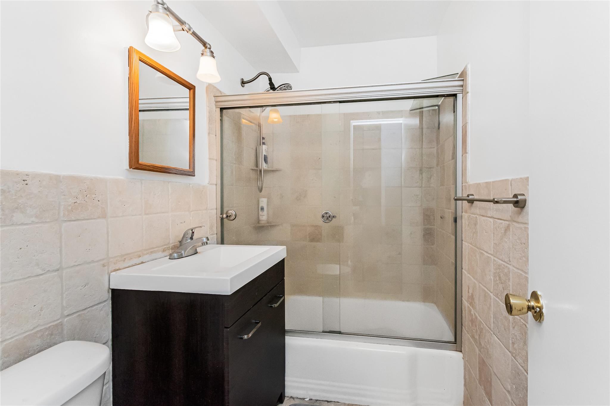 Full bath with vanity, tile walls, toilet, and combined bath / shower with glass door