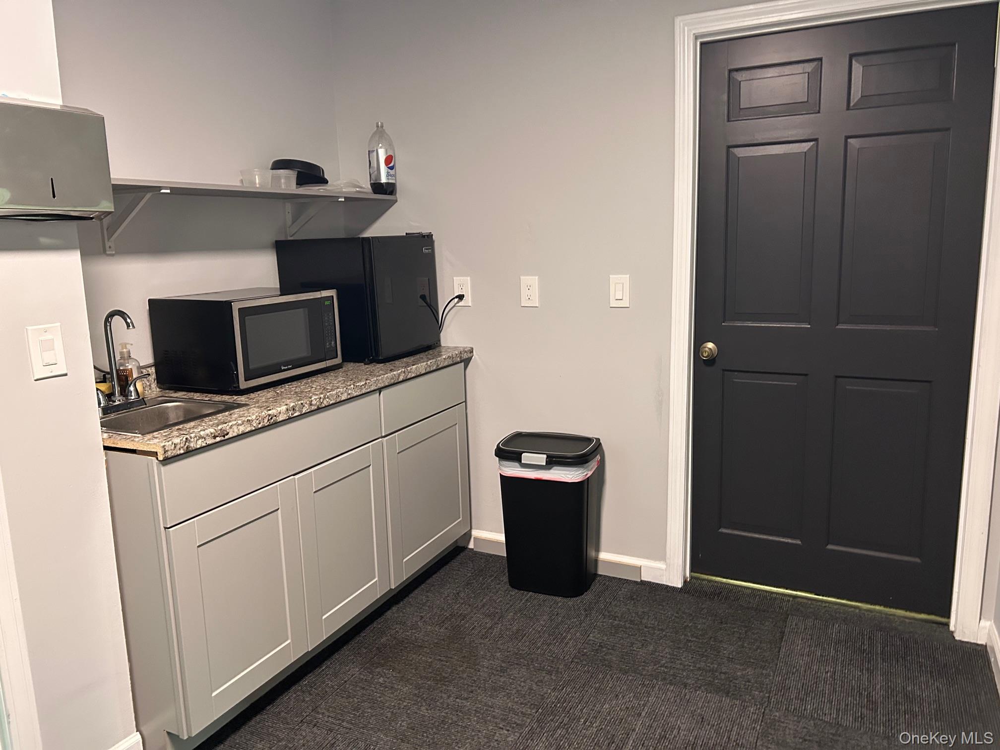 Kitchen with a sink, dark carpet, open shelves, baseboards, and light countertops