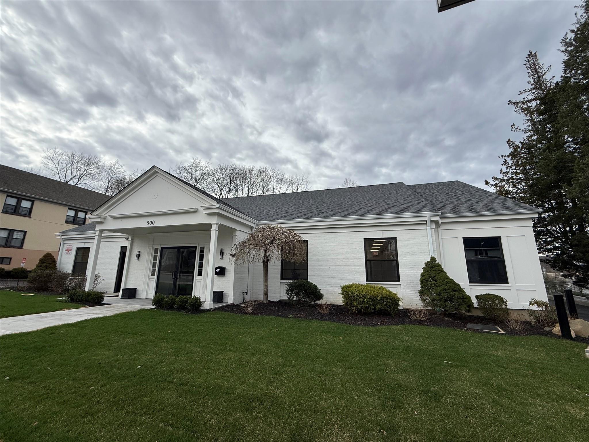 Neoclassical home with a front yard, roof with shingles, and brick siding