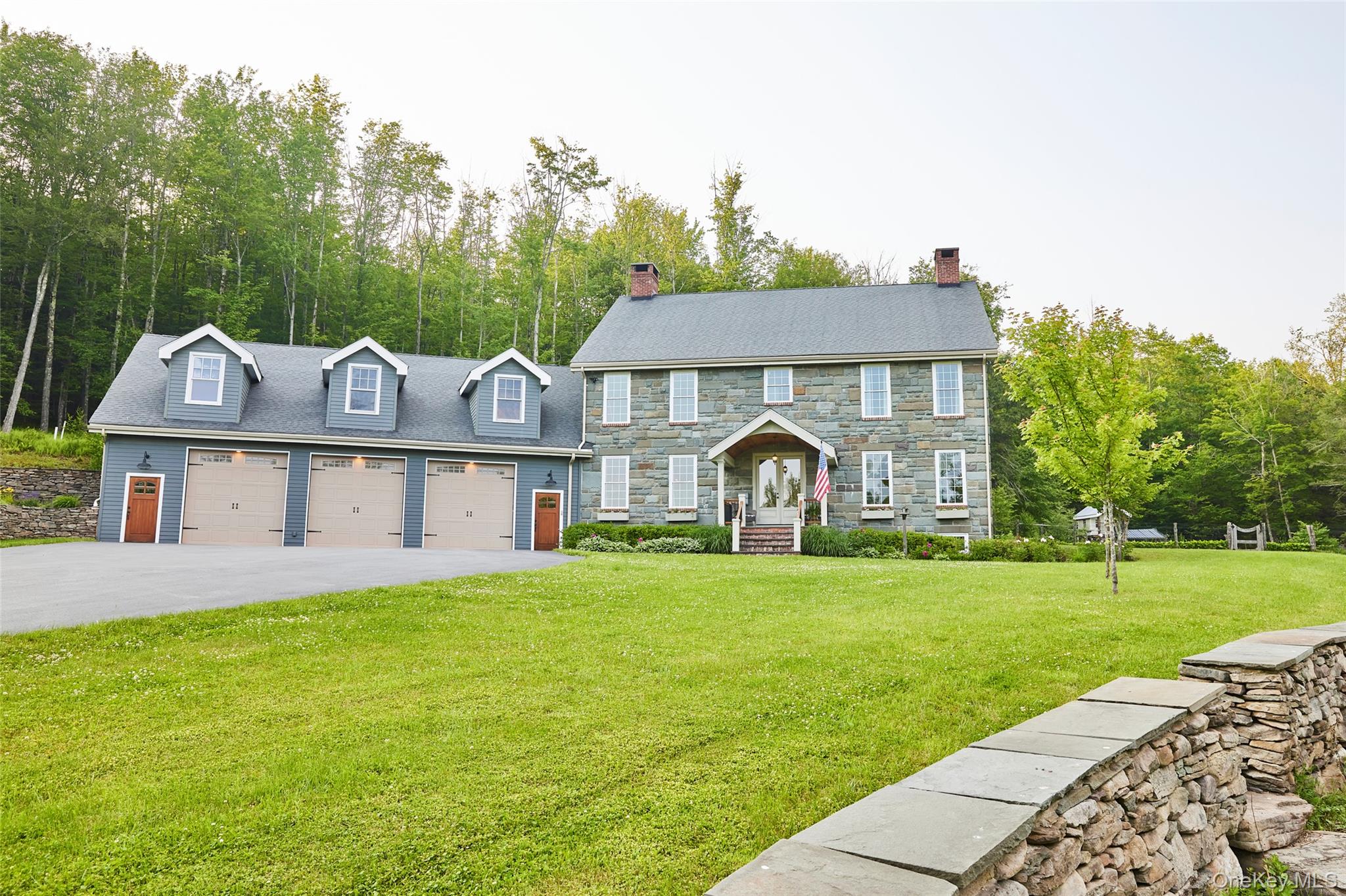 Colonial home with a front yard, a garage, a chimney, stone siding, and driveway