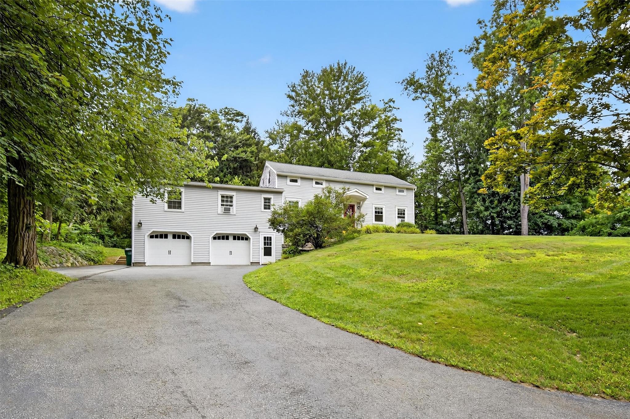 View of front of house featuring driveway, an attached garage, a front yard, and view of scattered trees