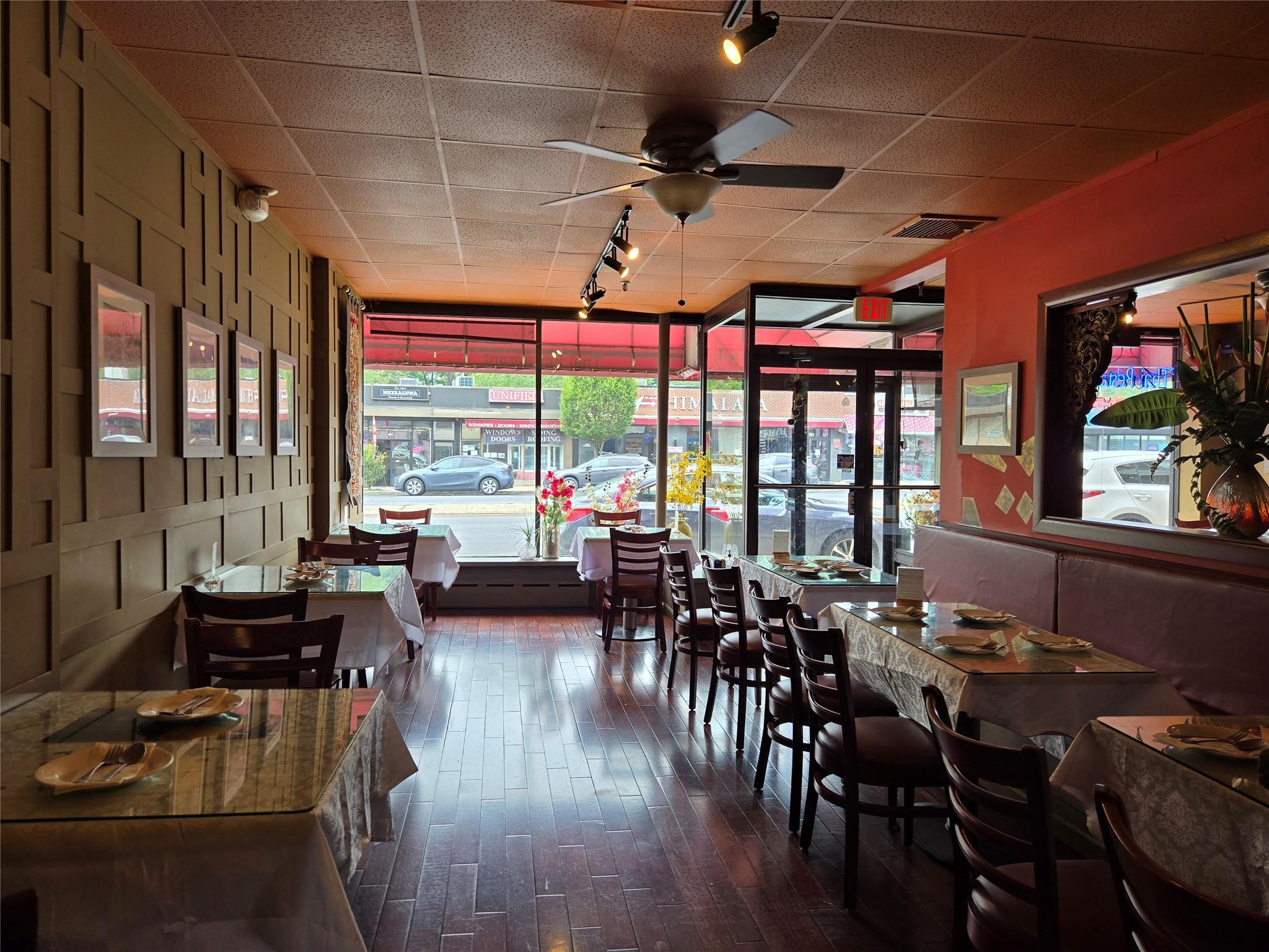 Dining space with track lighting, healthy amount of natural light, dark wood-type flooring, a ceiling fan, and a wall of windows