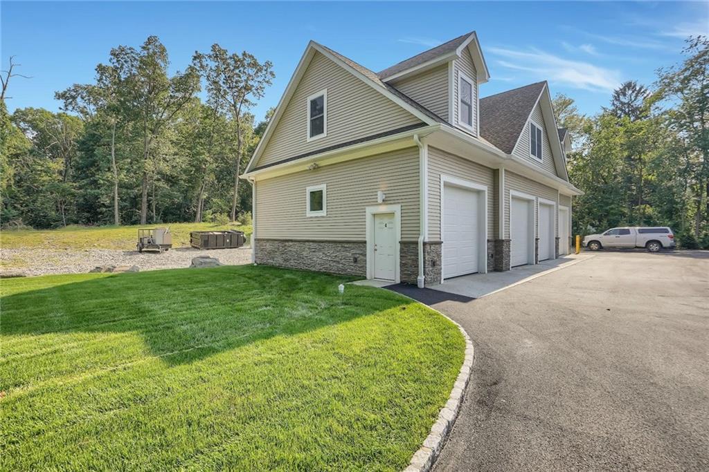 View of side of home with a lawn, asphalt driveway, stone siding, and an attached garage