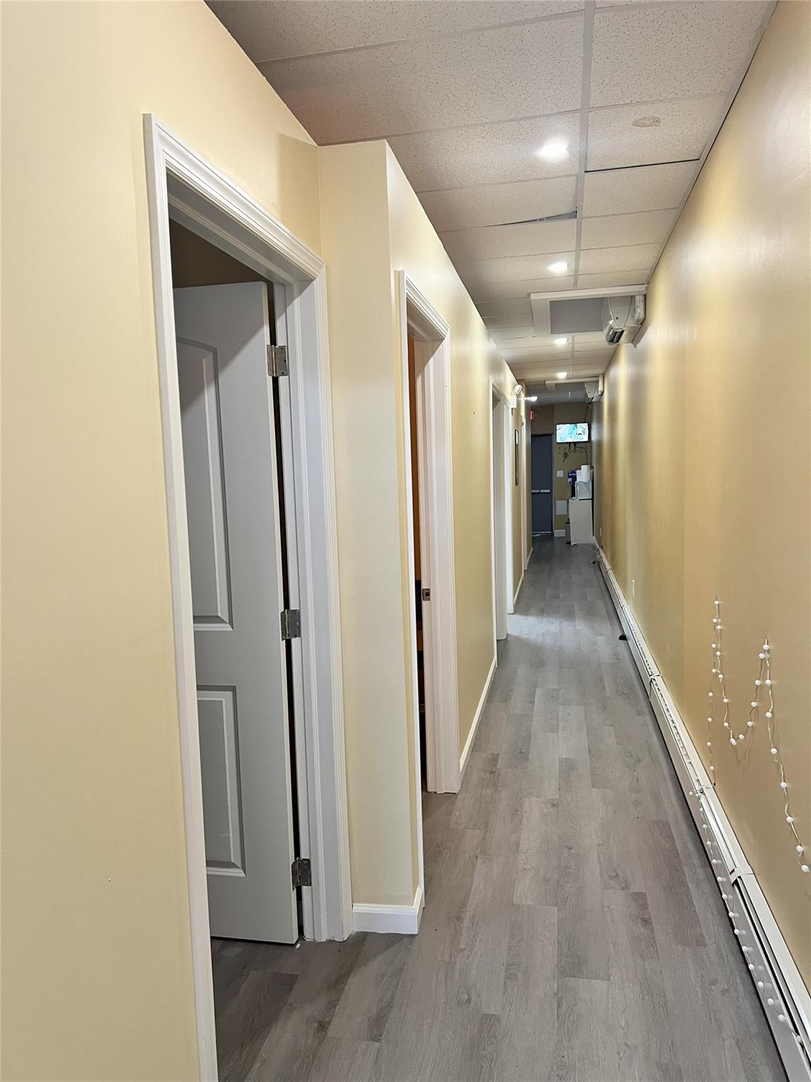 Corridor with baseboard heating, wood finished floors, and a paneled ceiling