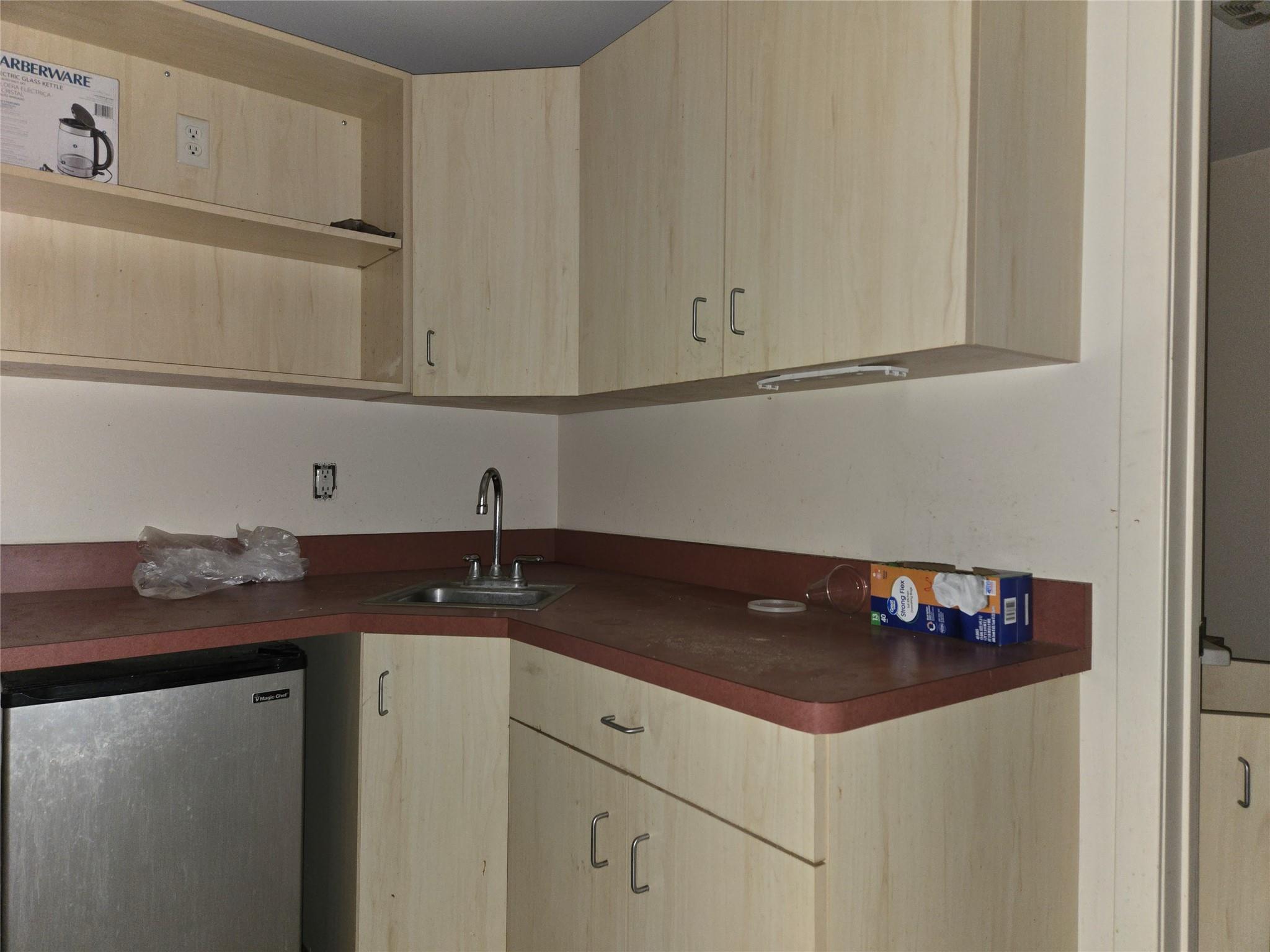Kitchen with light brown cabinets, dark countertops, and fridge