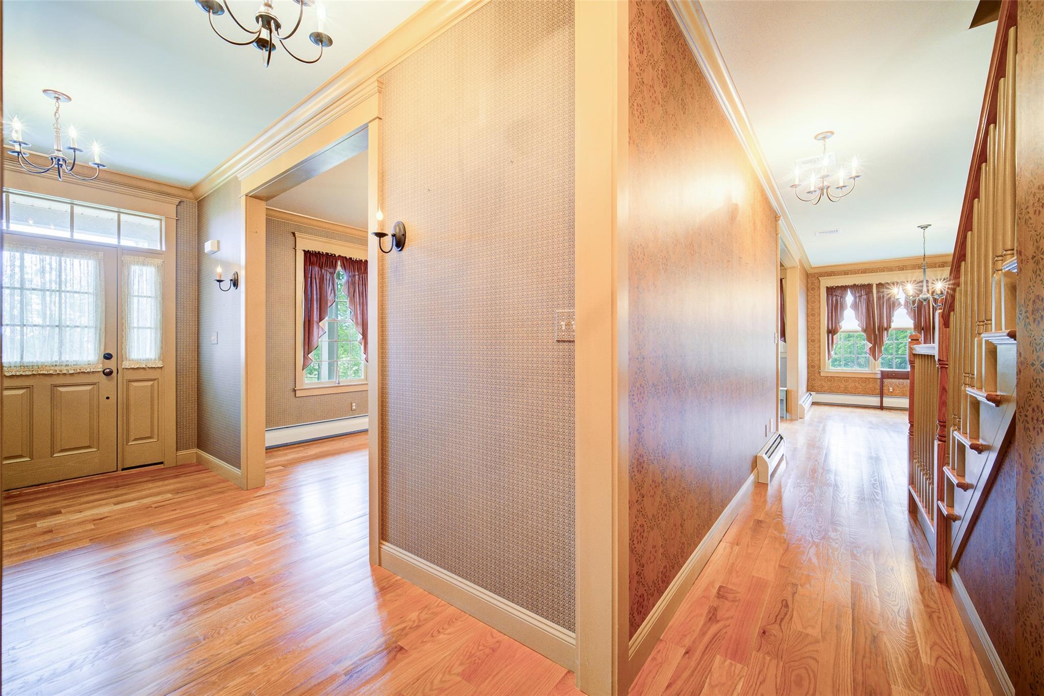 Hall with a chandelier, baseboard heating, crown molding, healthy amount of natural light, and light wood-style flooring