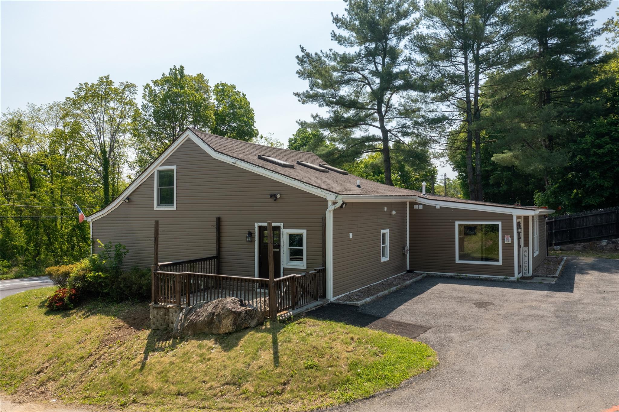 Back of property with a wooden deck, driveway, a shingled roof, and a lawn