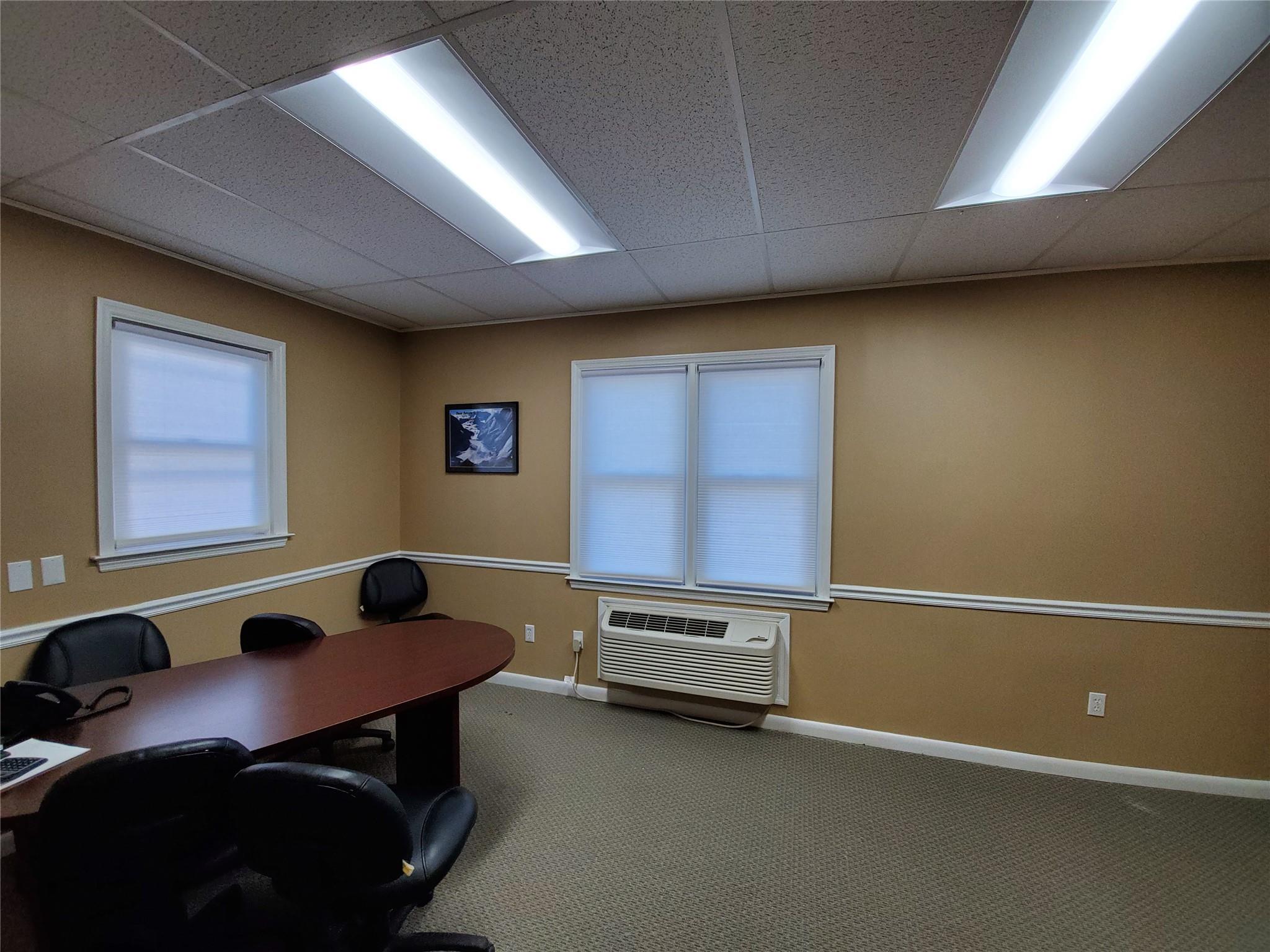 Carpeted home office featuring a drop ceiling, plenty of natural light, and a wall mounted AC