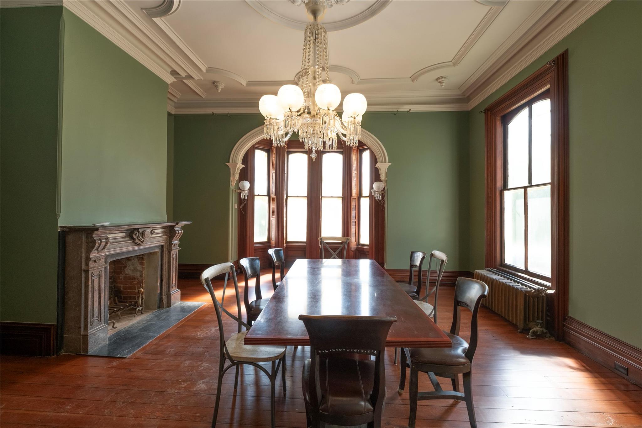 Dining room featuring a chandelier, radiator, wood-type flooring, a fireplace, and ornamental molding