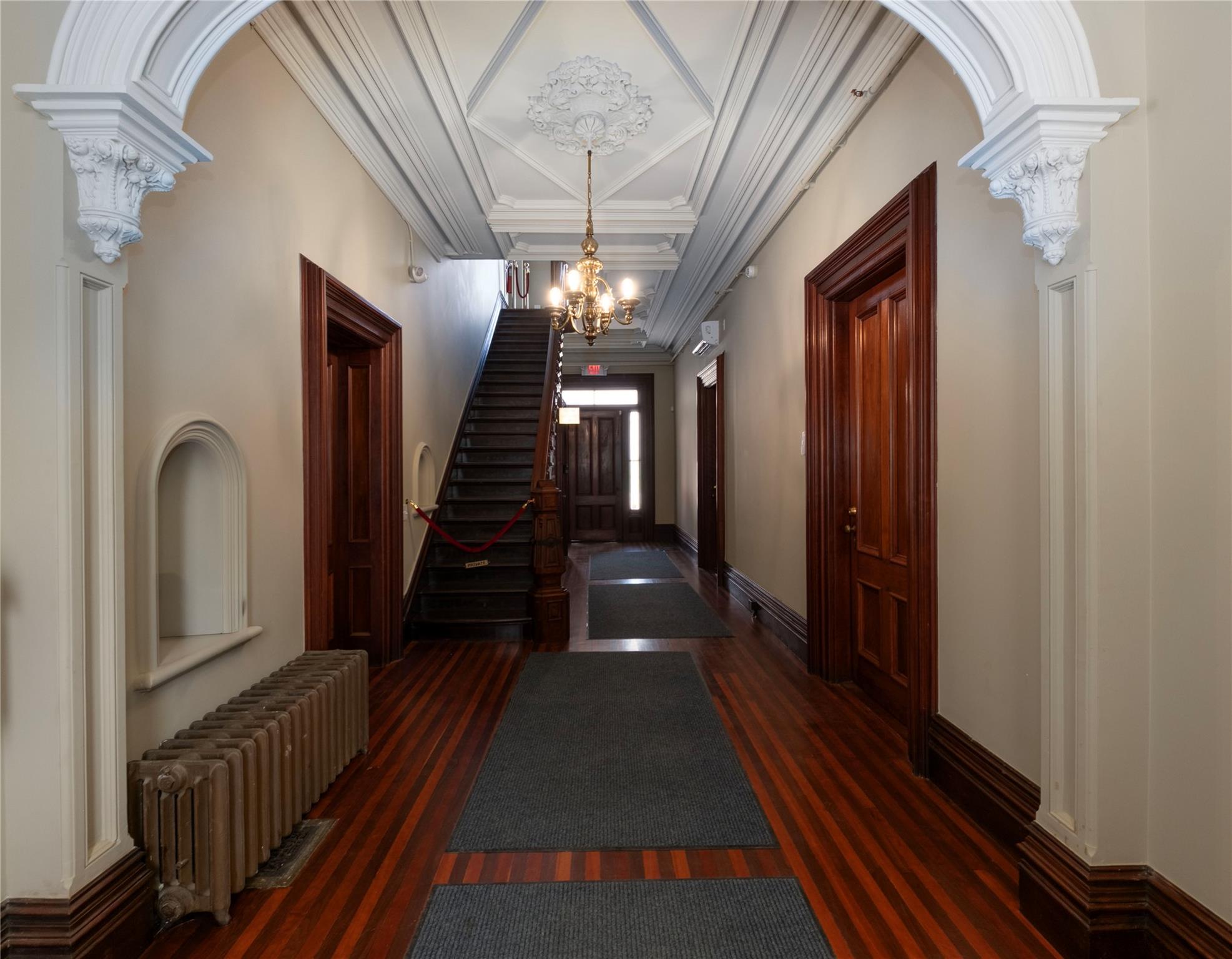 Hallway featuring radiator, a chandelier, wood finished floors, ornamental molding, and stairway