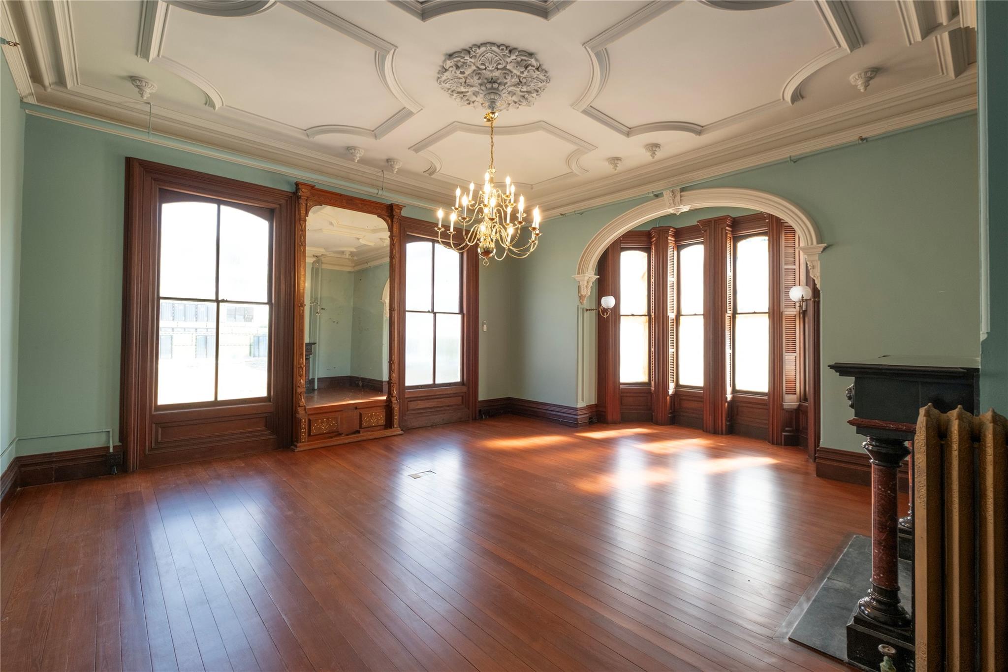 Unfurnished room featuring a chandelier, hardwood / wood-style floors, radiator heating unit, arched walkways, and crown molding