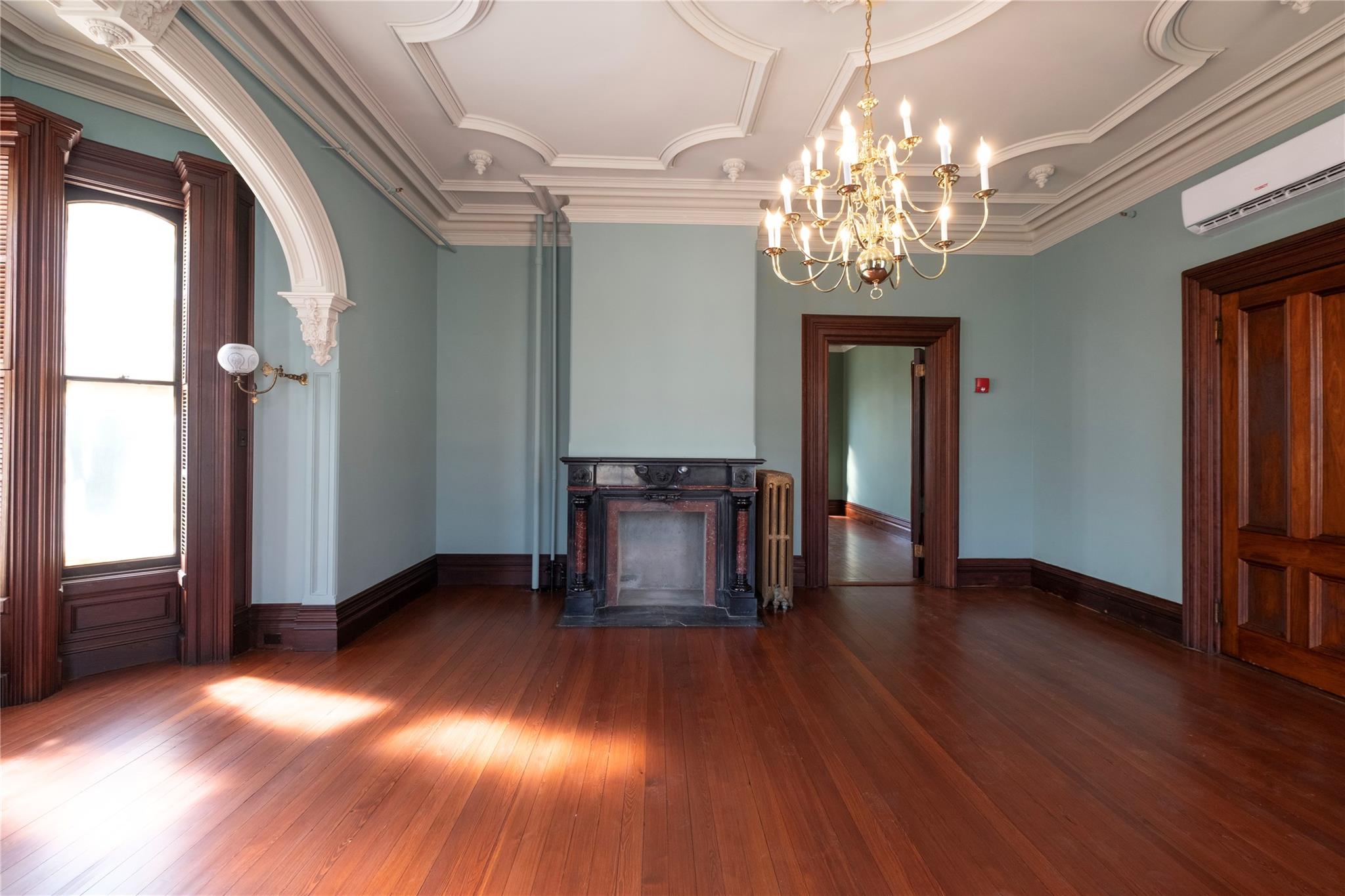 Unfurnished living room featuring a high end fireplace, wood-type flooring, a wall unit AC, a chandelier, and crown molding