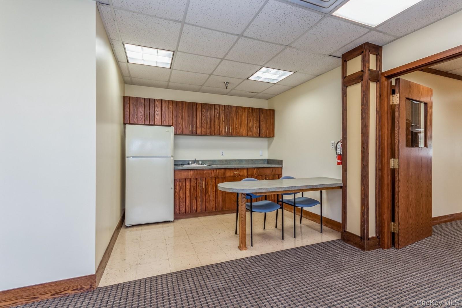 Kitchen with a drop ceiling, freestanding refrigerator, light flooring, and brown cabinets