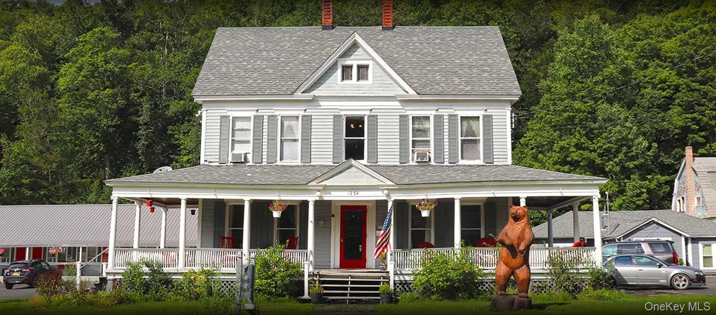 View of front facade with covered porch, roof with shingles, and a view of trees