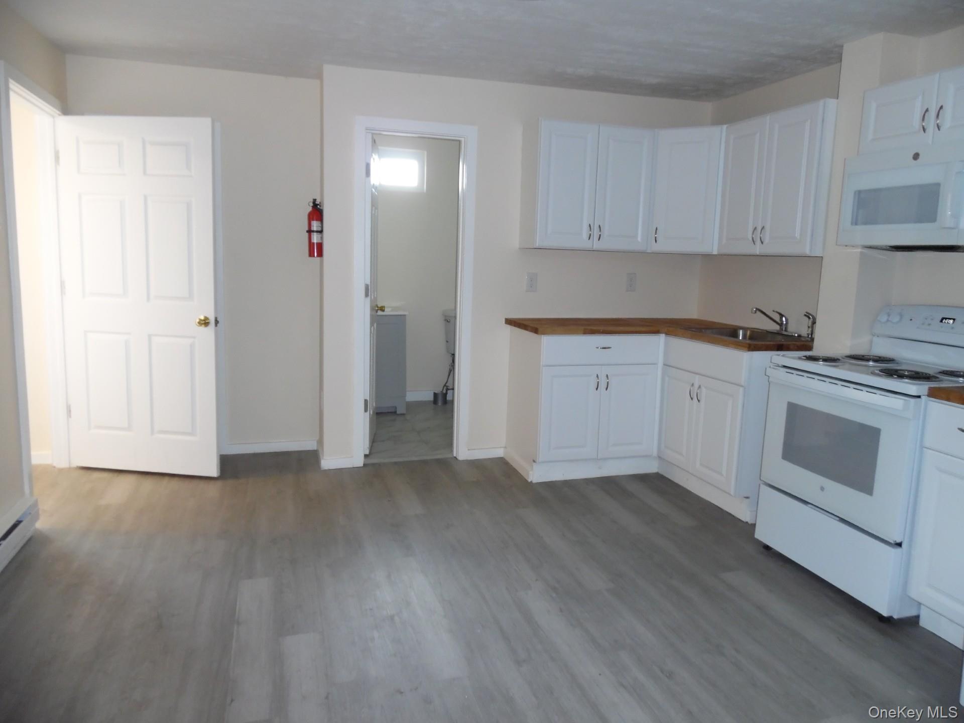 Kitchen with white appliances, dark wood-style flooring, white cabinetry, and butcher block countertops