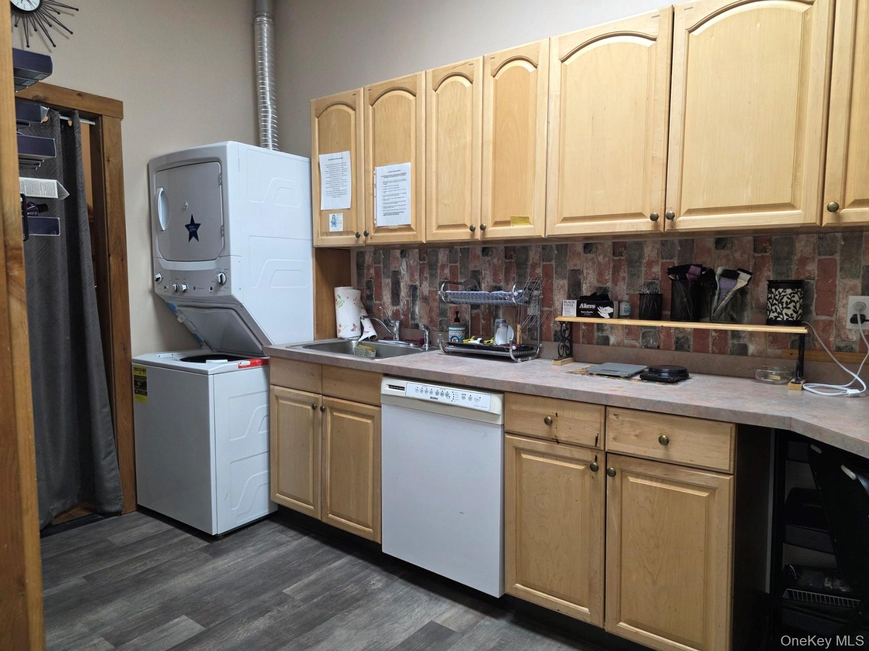 Kitchen featuring backsplash, light countertops, white dishwasher, dark wood finished floors, and estacked washer and dryer