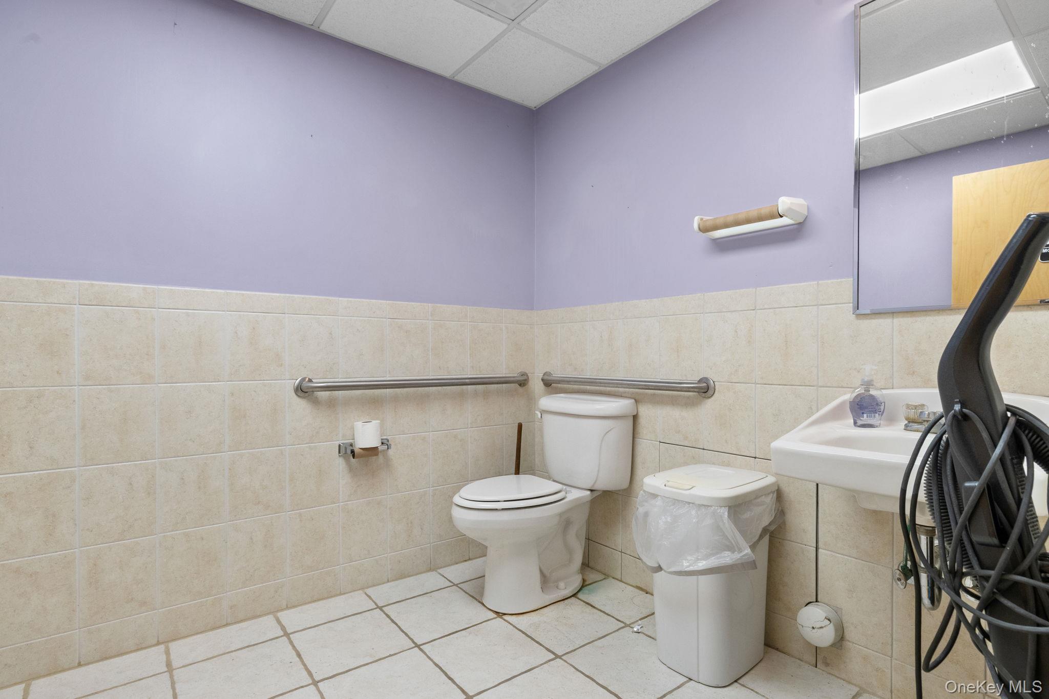 Half bath with a drop ceiling, tile patterned flooring, tile walls, and a wainscoted wall
