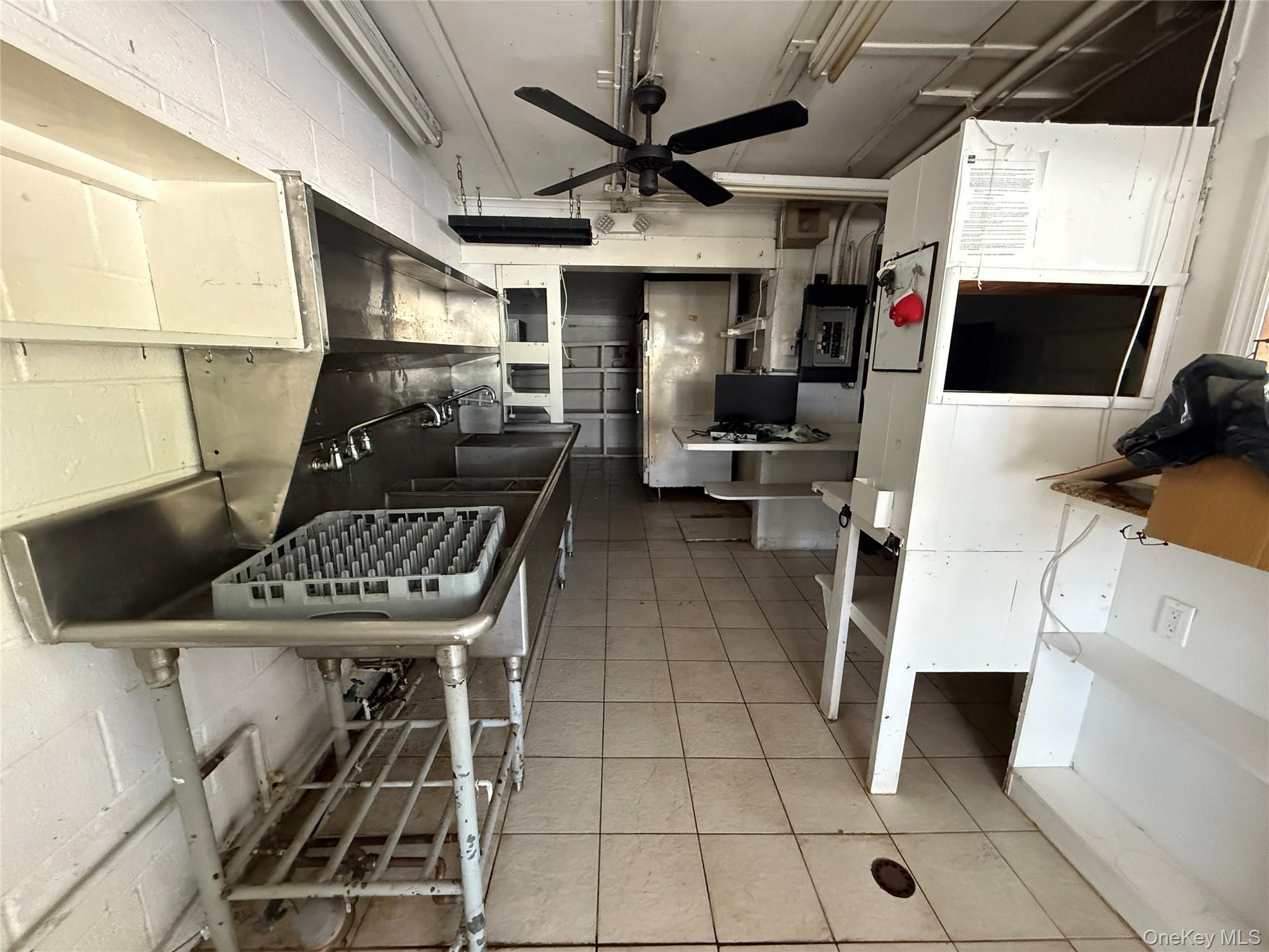 Kitchen with a ceiling fan, light tile patterned floors, electric panel, and concrete block wall