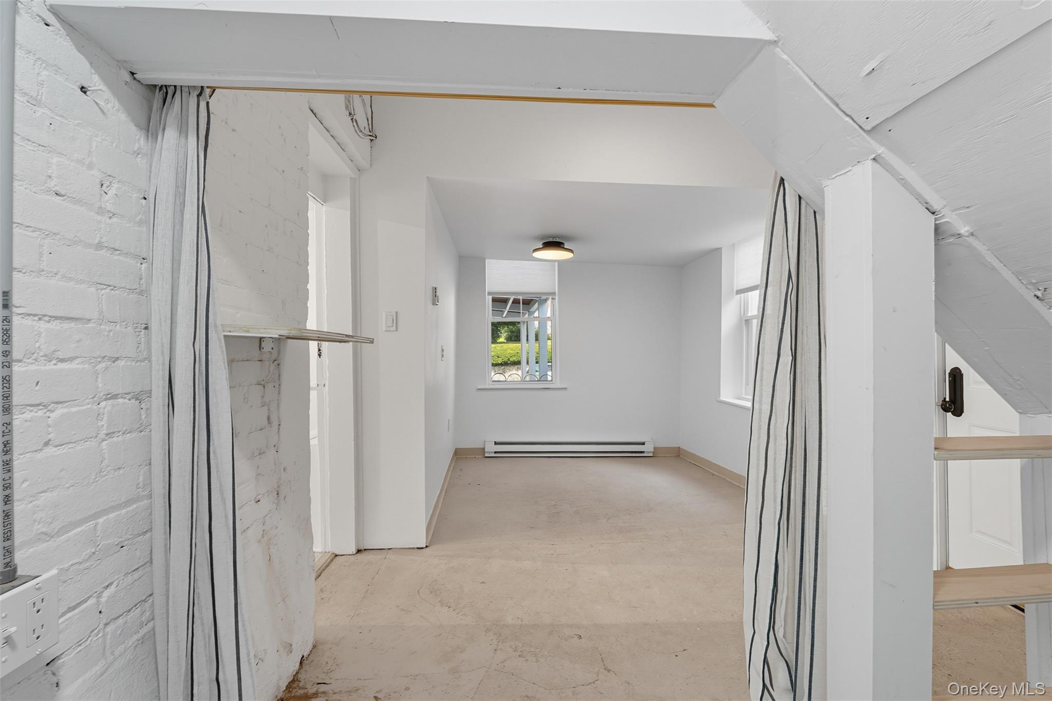 Hall with unfinished concrete flooring and a baseboard heating unit