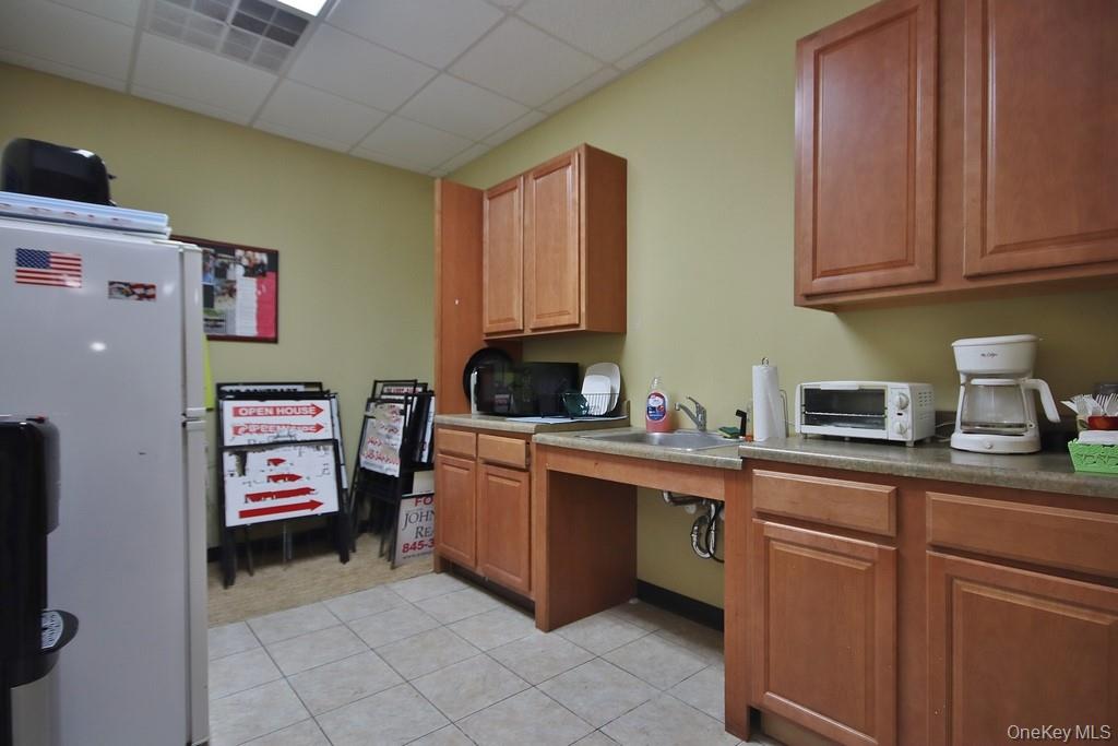 Kitchen featuring white refrigerator, brown cabinets and light tile patterned flooring.