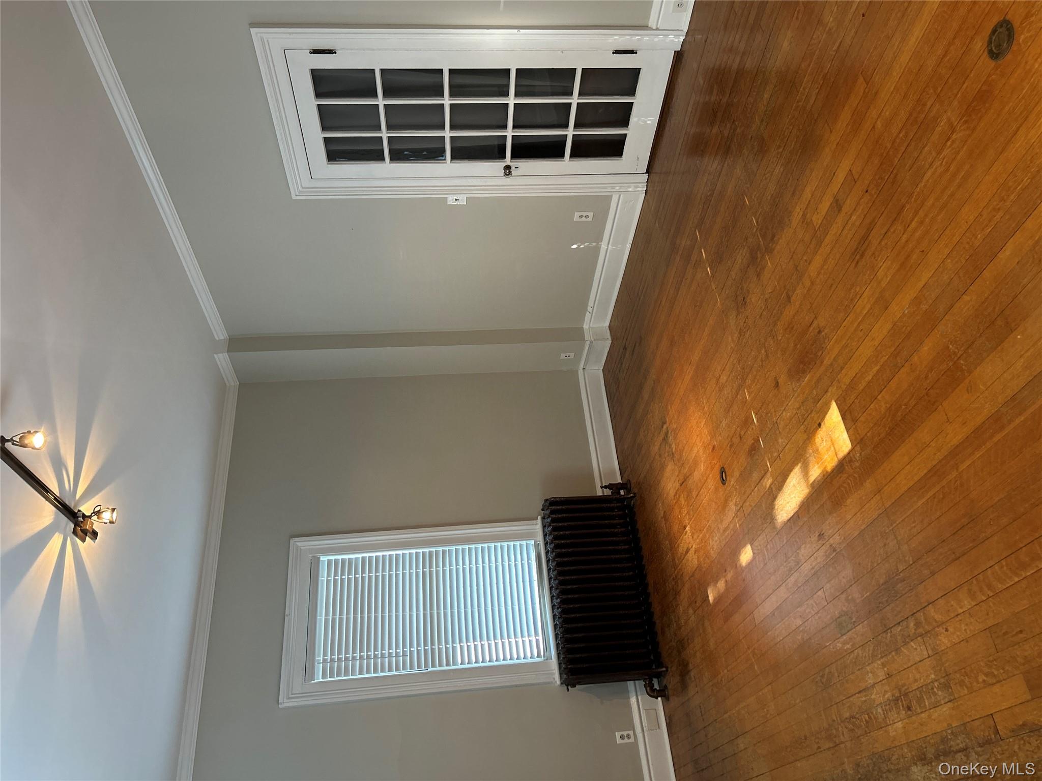Empty room with ornamental molding, dark wood finished floors, and radiator heating unit
