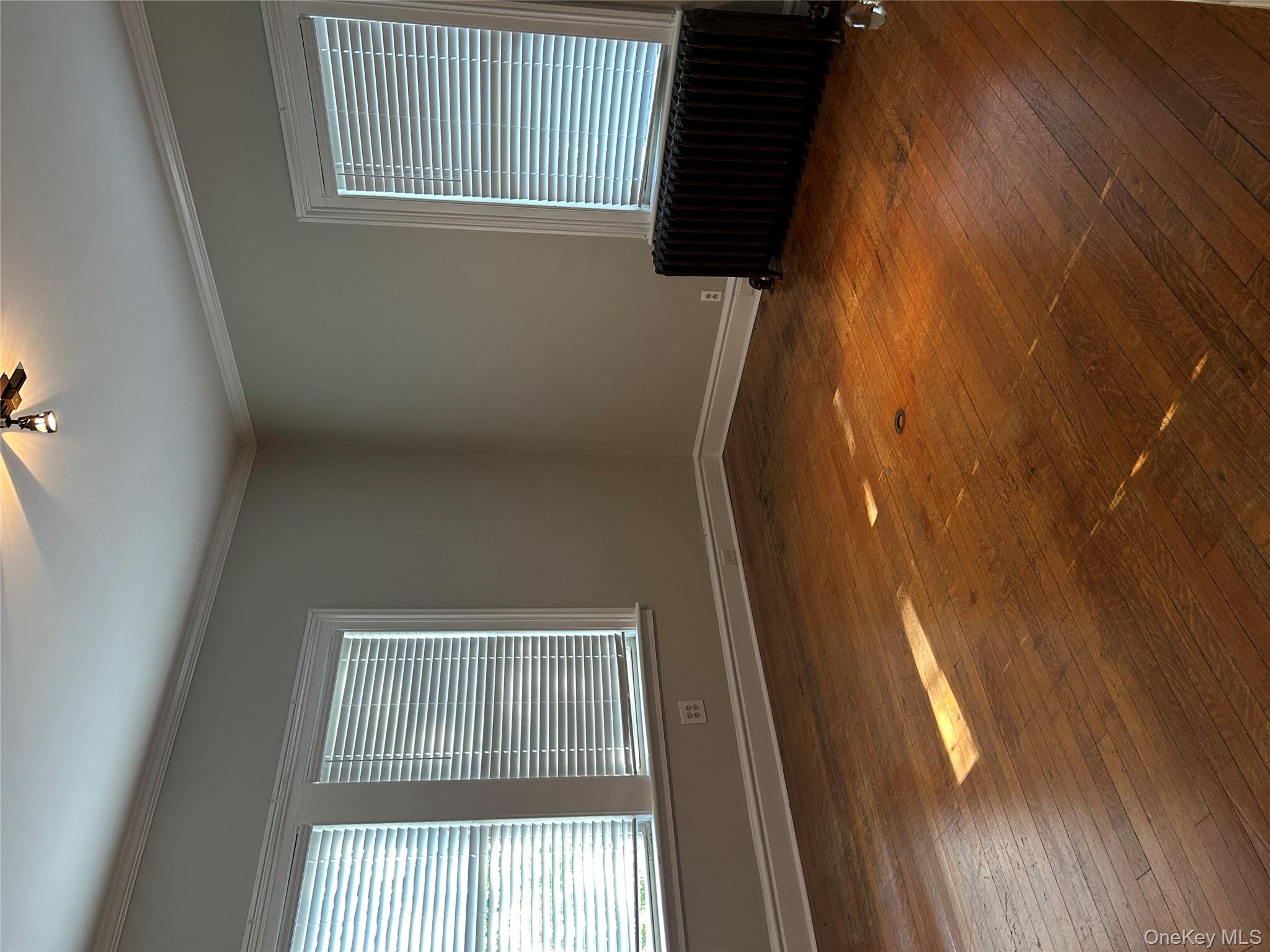Empty room featuring radiator heating unit, dark wood-style flooring, and crown molding