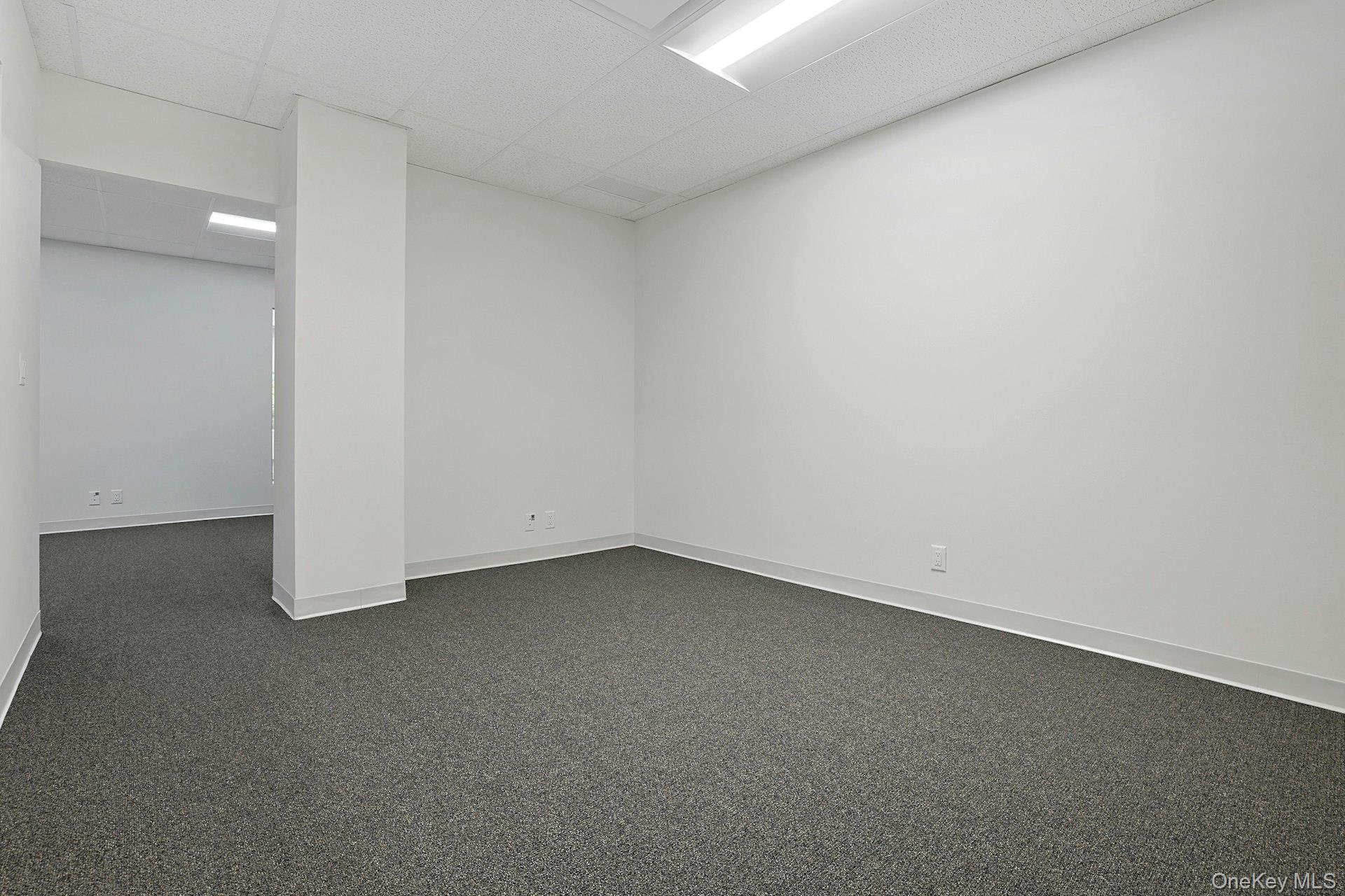 Empty room featuring a paneled ceiling and dark carpet