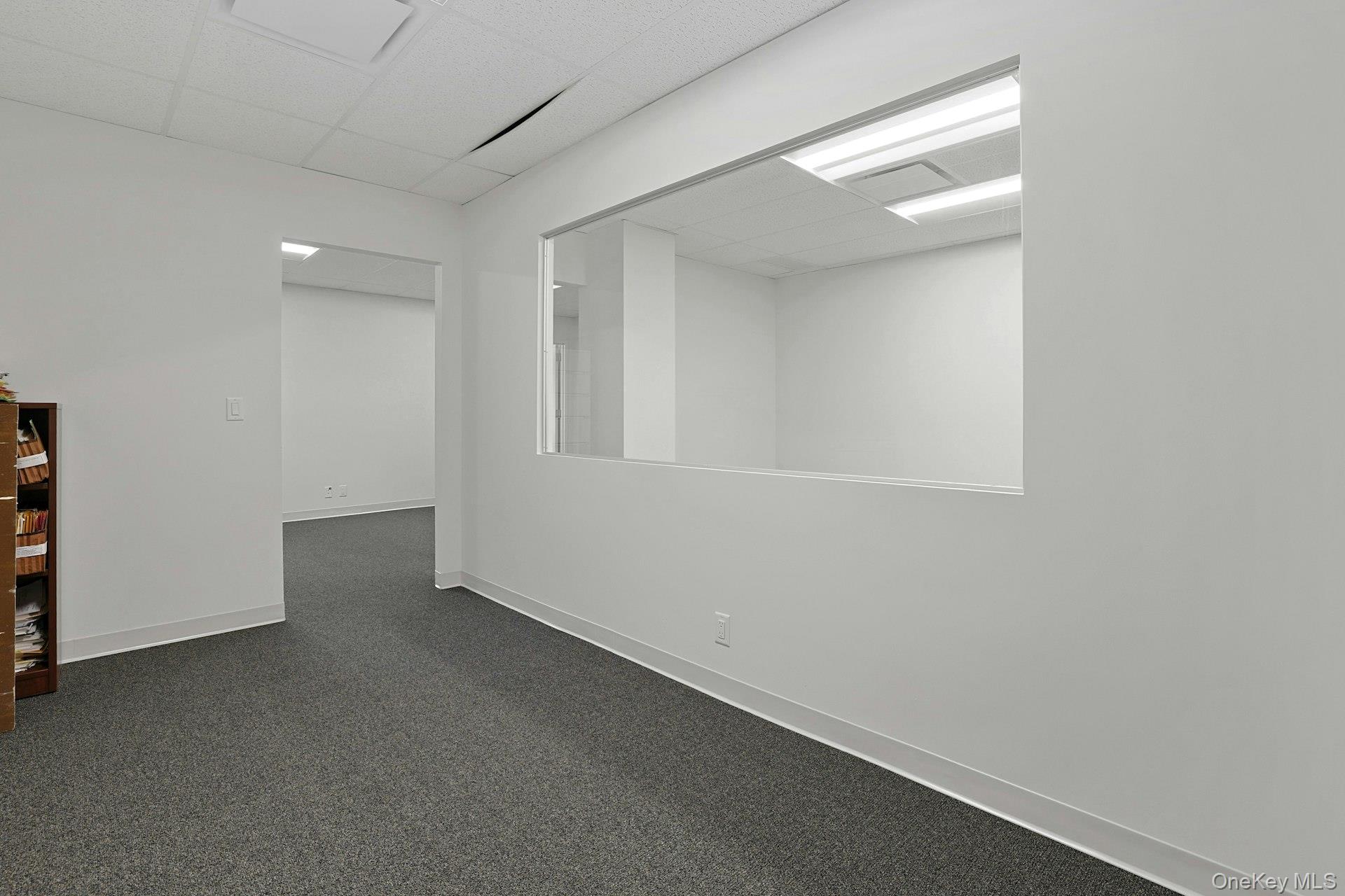 Empty room with a paneled ceiling and dark colored carpet