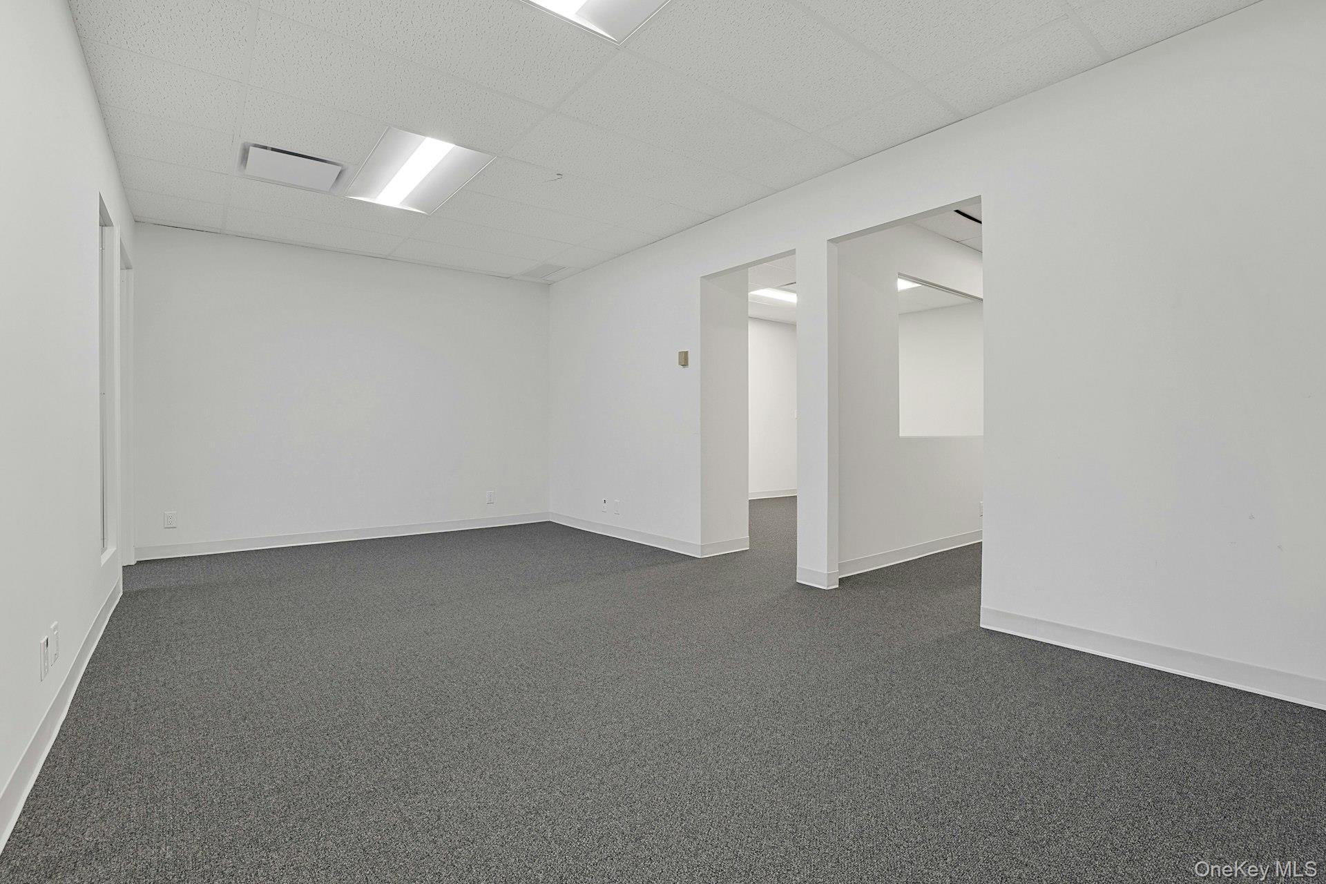 Spare room with a drop ceiling and dark colored carpet
