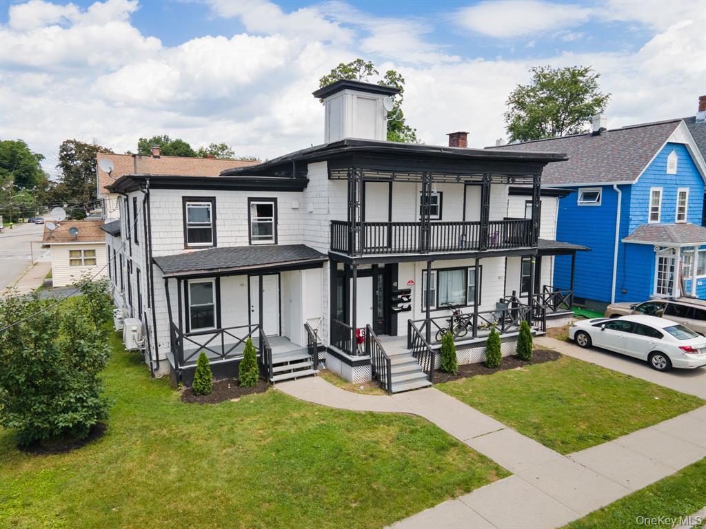 View of front of property with a chimney, a porch, a balcony, a front yard, and roof with shingles