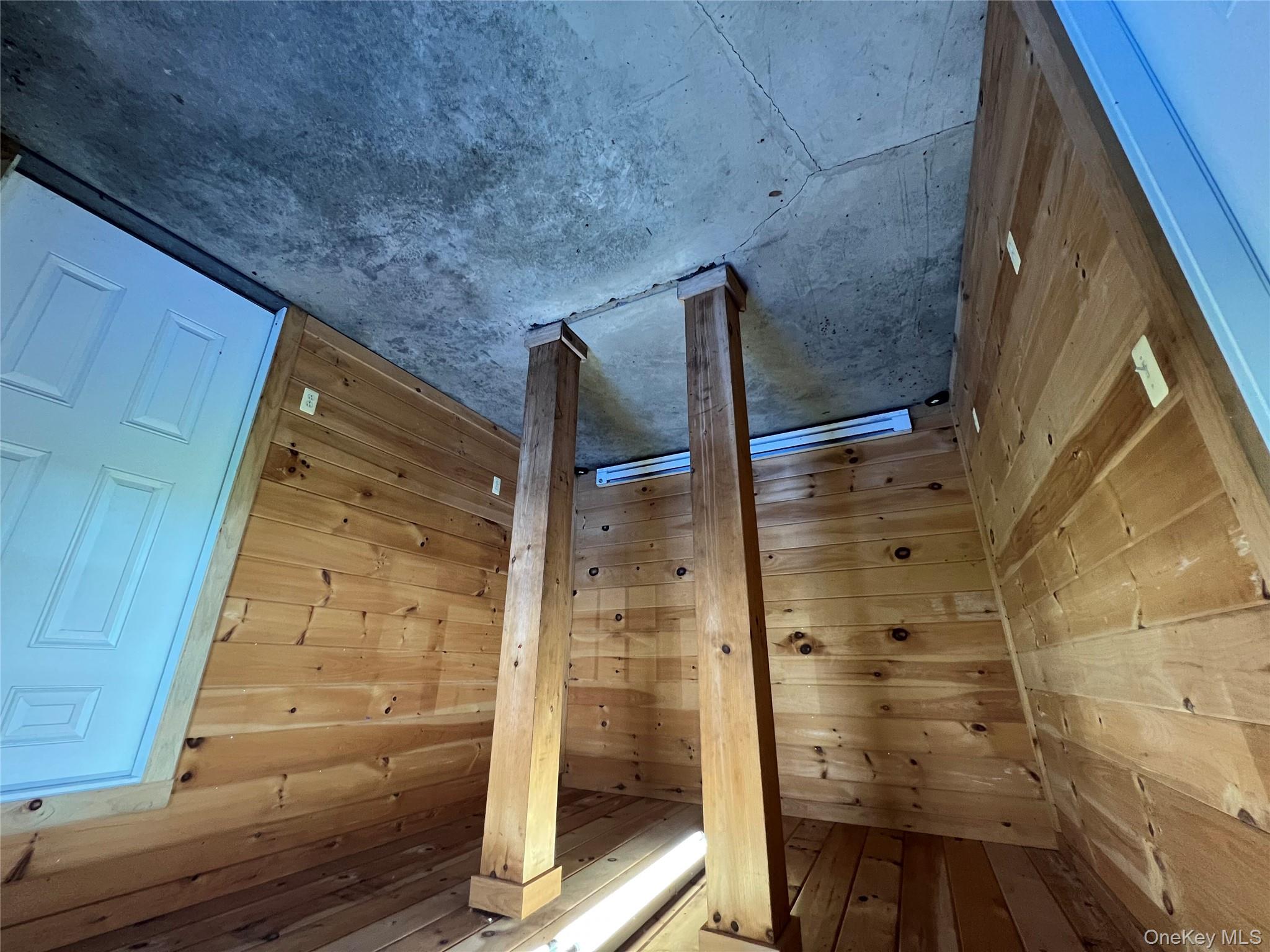 Additional living space with unfinished concrete floors, baseboard heating, and wood walls